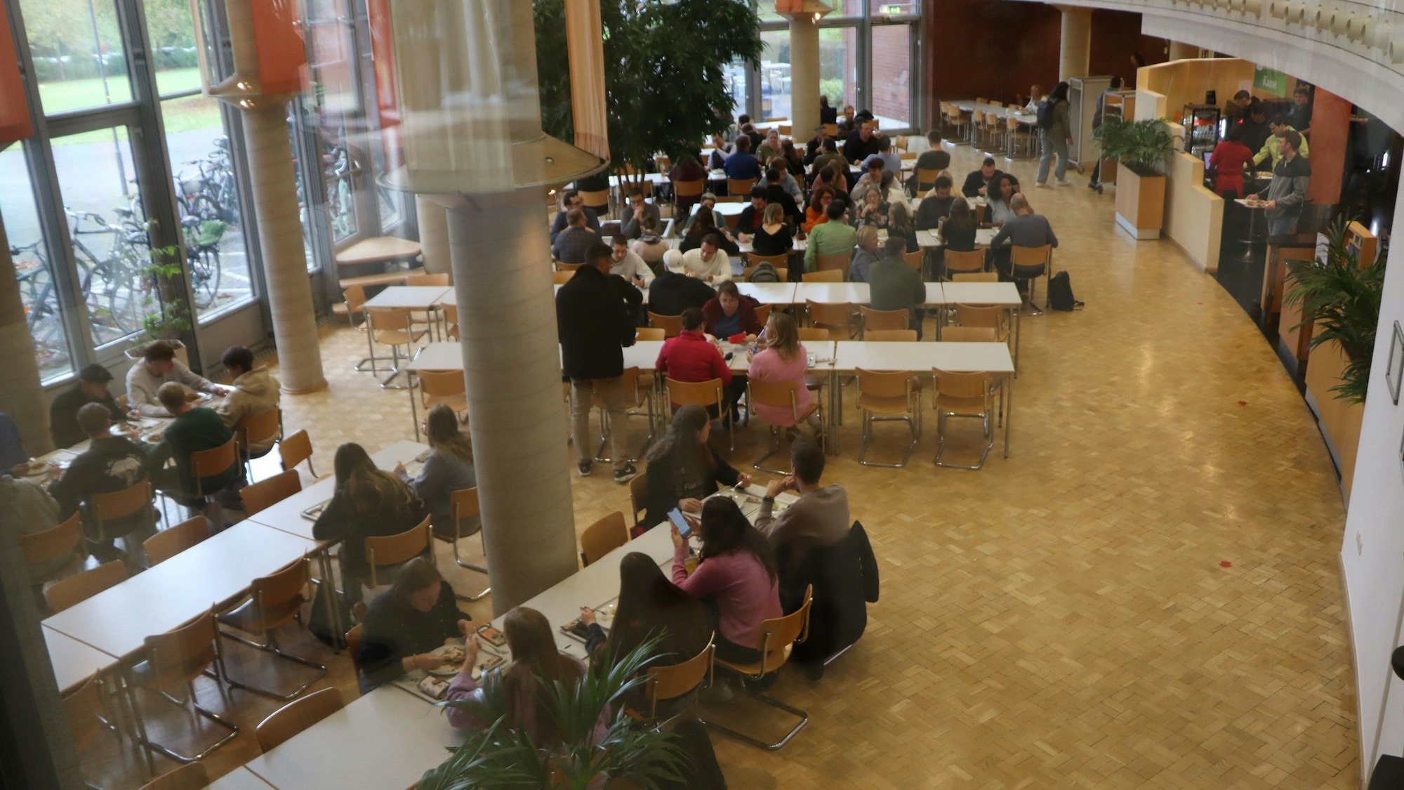 Blick in die Kantine, wo Frauen und Männer an Tischen sitzen.