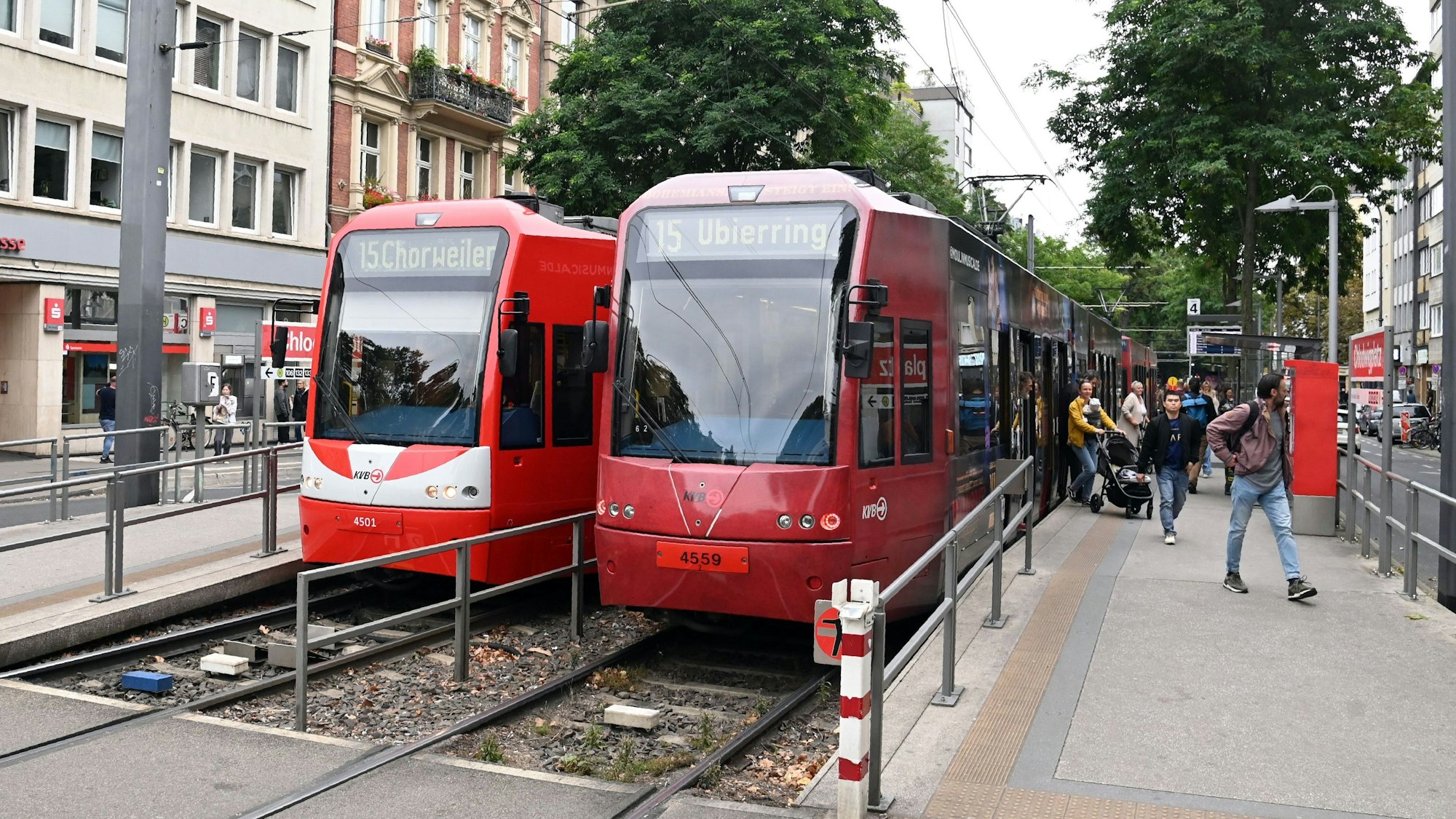 Zu sehen sind zwei Bahnen der KVB in der Vorderansicht. Links davon steigen Fahrgäste ein und aus.