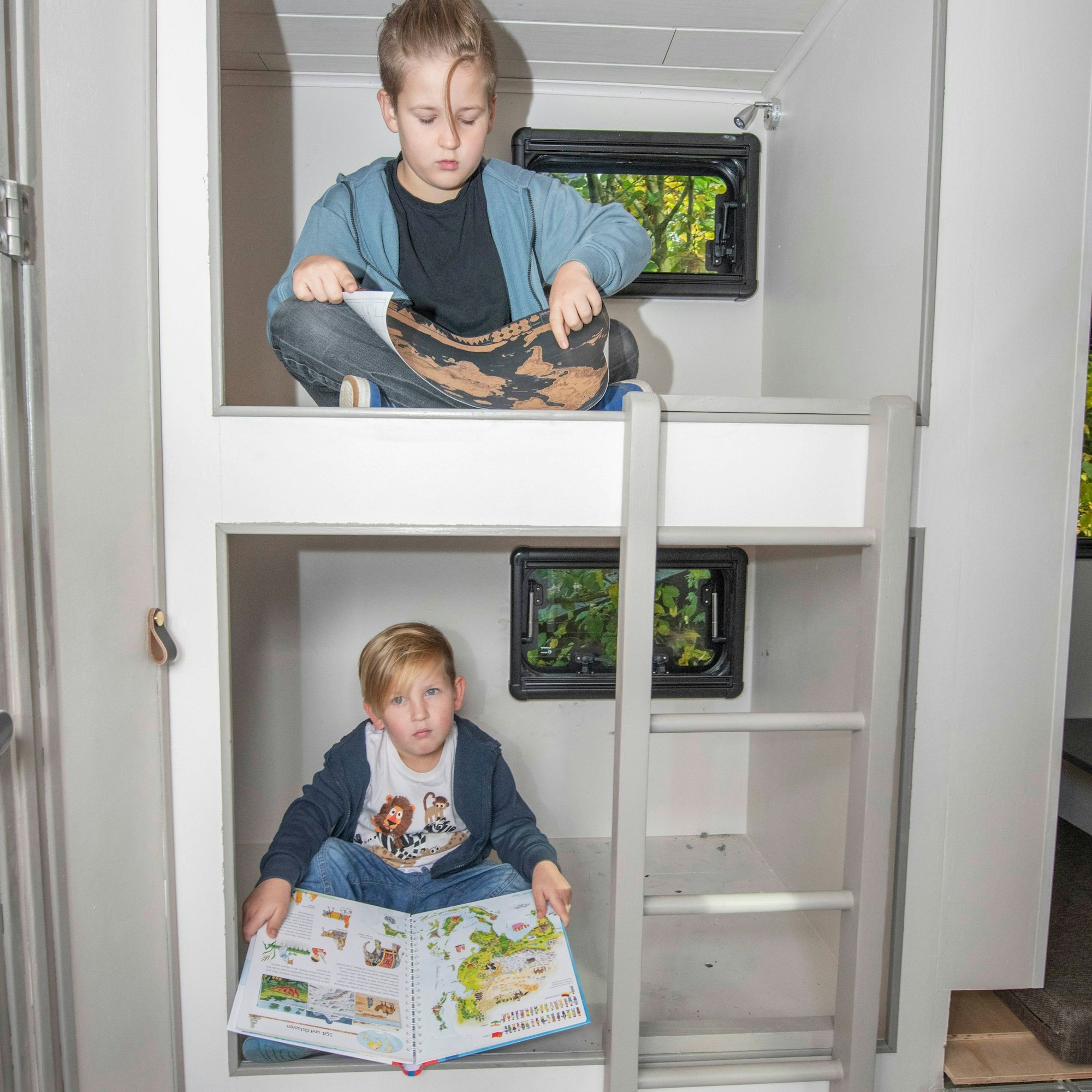 Zwei Jungs sitzen im Hochbett eines ausgebauten Expeditionsmobils.