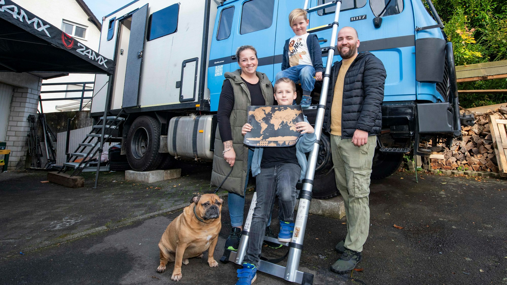 Familie Pollkläsener aus Gummersbach steht vor einem Expeditionsmobil mit hellblauem Führerhaus.