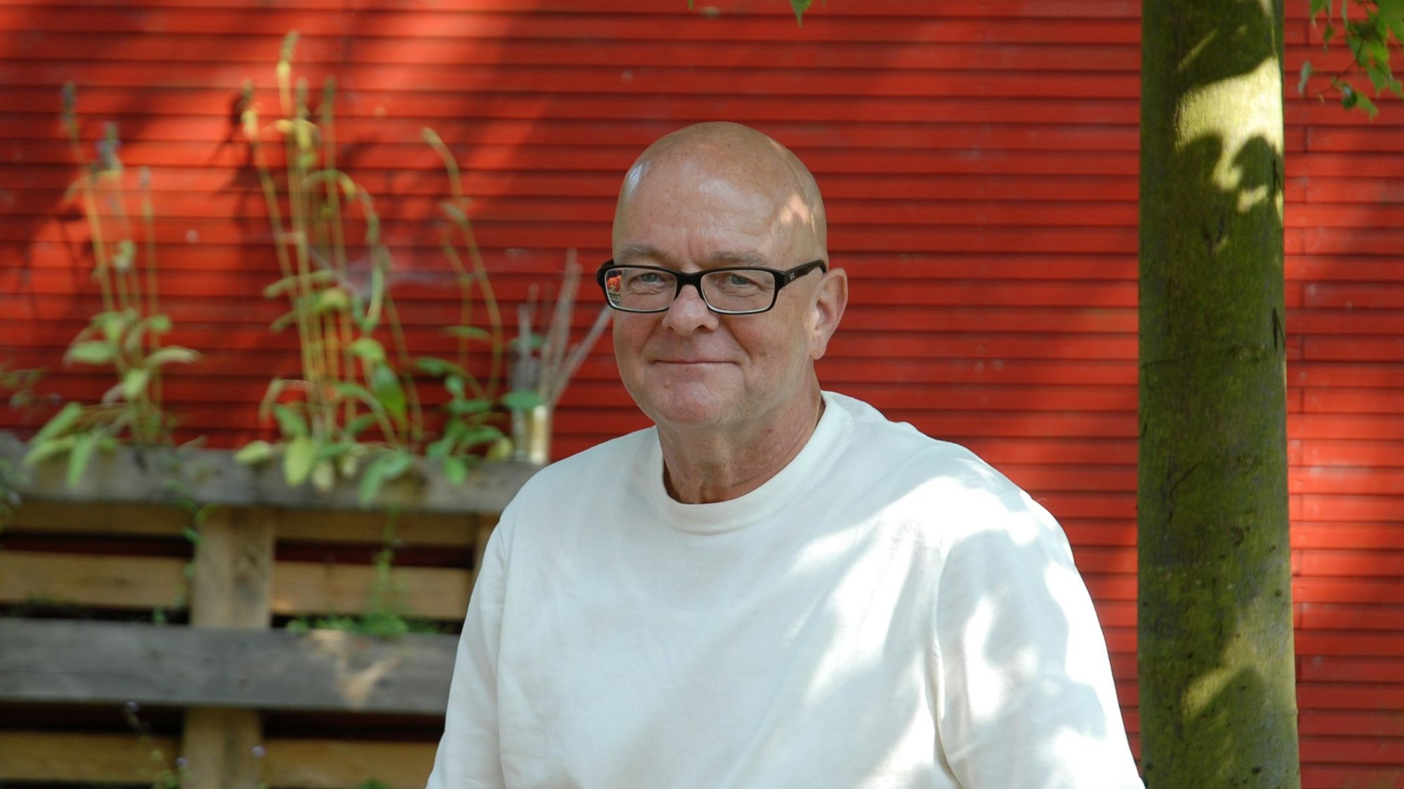 Ein Mann sitzt im Freien vor einer roten Wand.