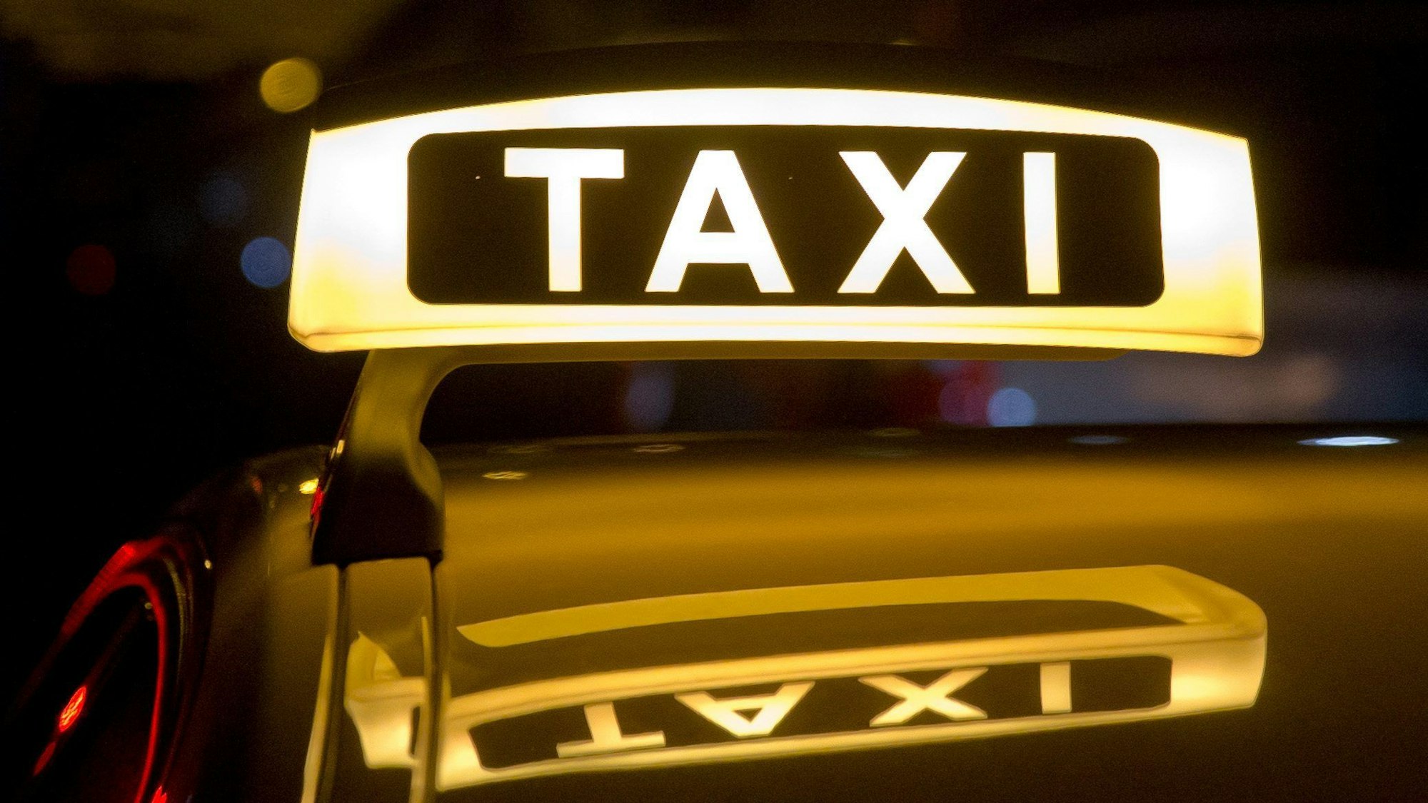 Ein beleuchtetes Taxi-Schild auf einem Autodach.