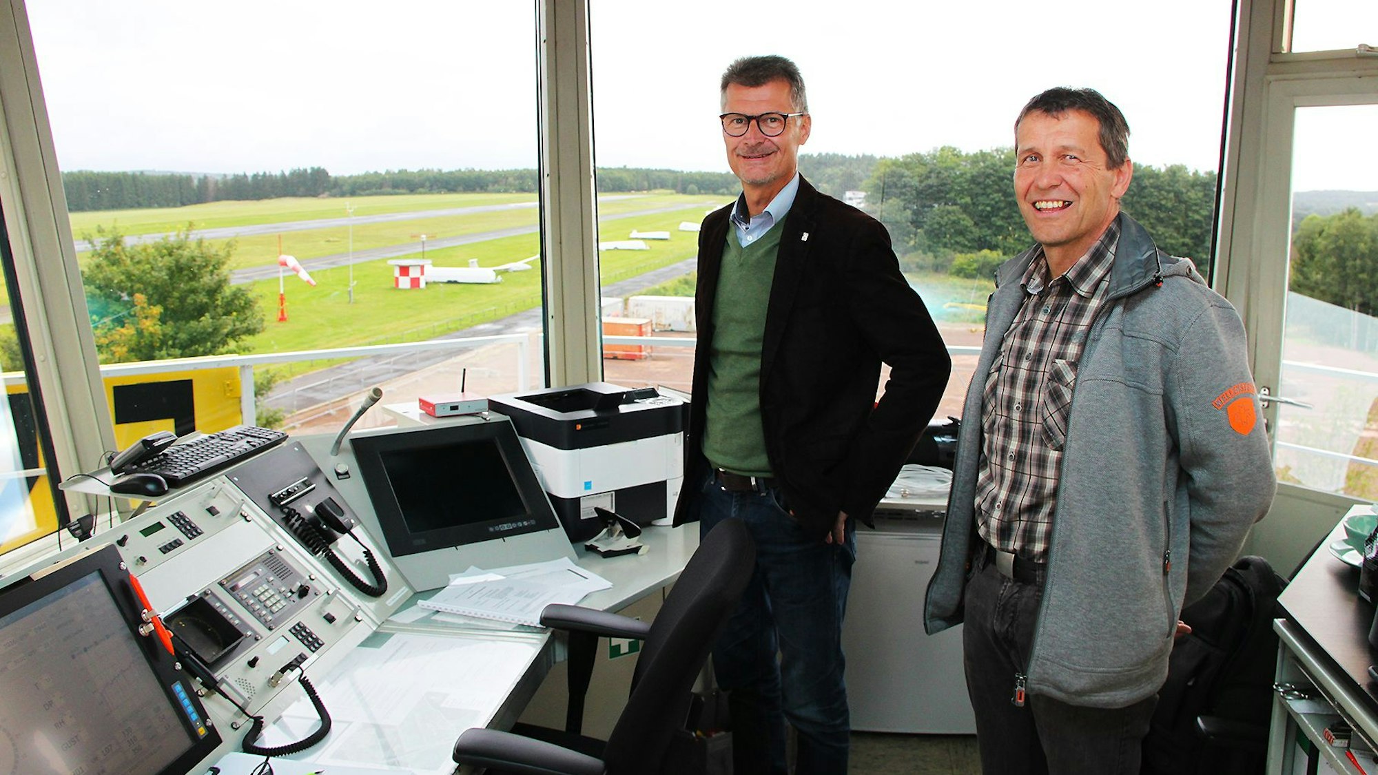 Die Geschäftsführer der Flugplatz GmbH, Jan Lembach (l.) und Erwin Bungartz, stehen im Tower der Dahlemer Binz. Durch die Fenster sind die Start- und Landebahnen zu sehen.