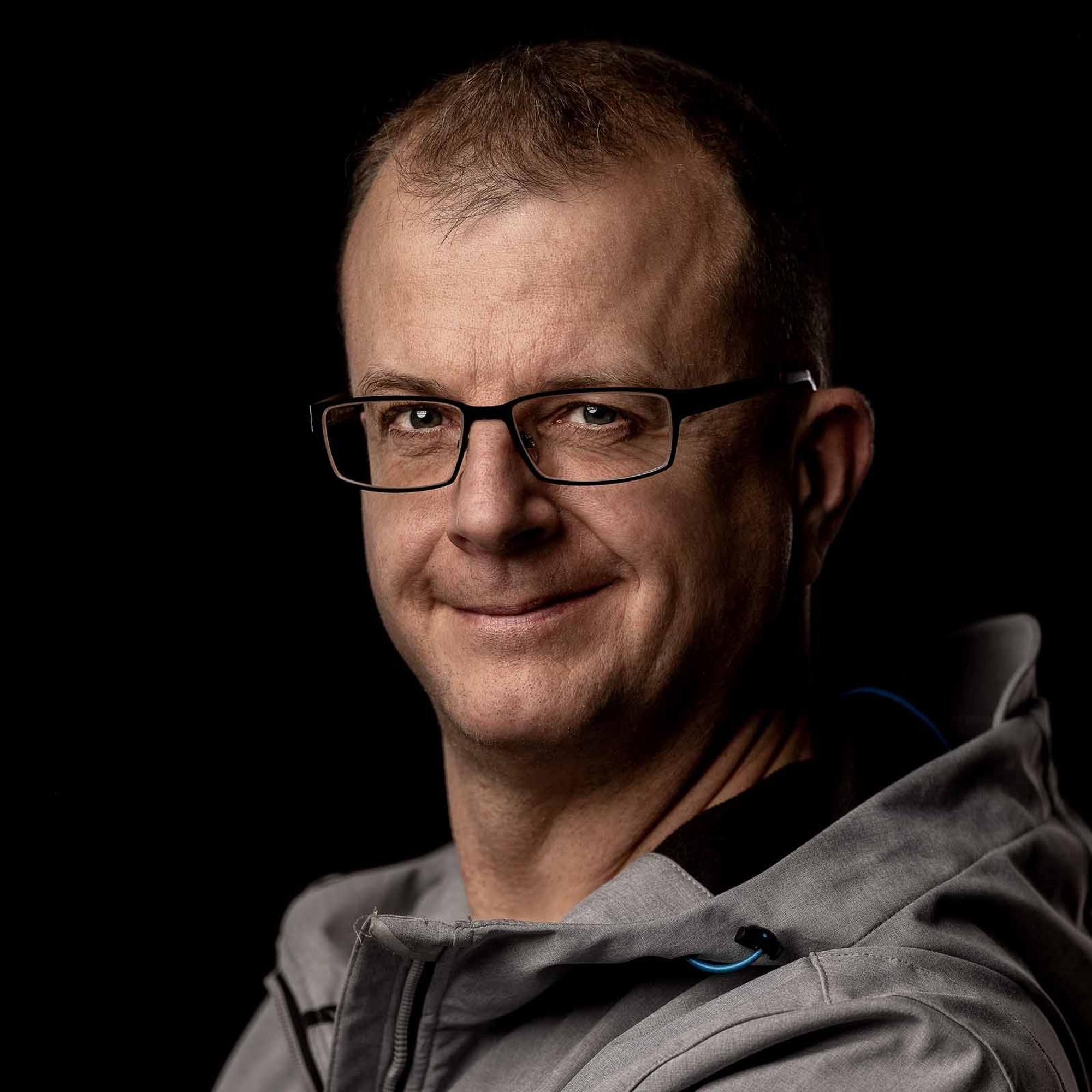 Stephan Habscheid trägt eine Brille und eine graue Jacke. Er lächelt in die Kamera.