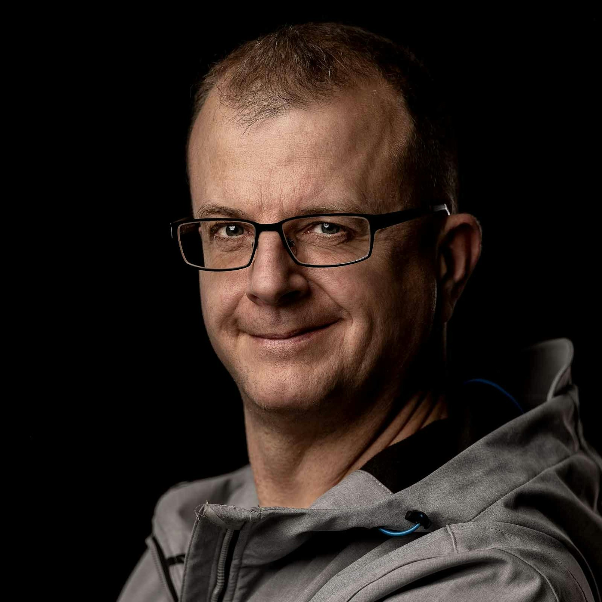 Stephan Habscheid trägt eine Brille und eine graue Jacke. Er lächelt in die Kamera.