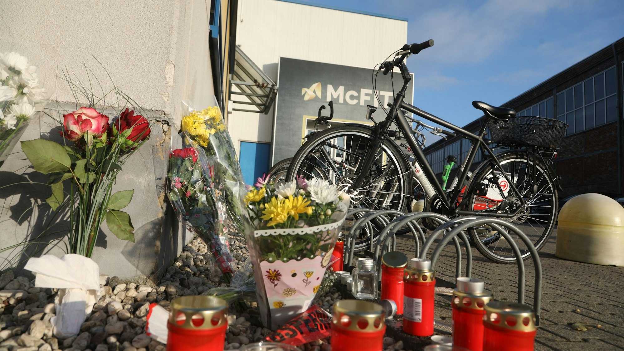 Blumen und Kerzen erinnern einen Tag später an den tödlichen Schuss, den ein Unbekannter auf einen 32-Jährigen vor dem Fitnessstudio in Köln-Kalk abgefeuert hat.