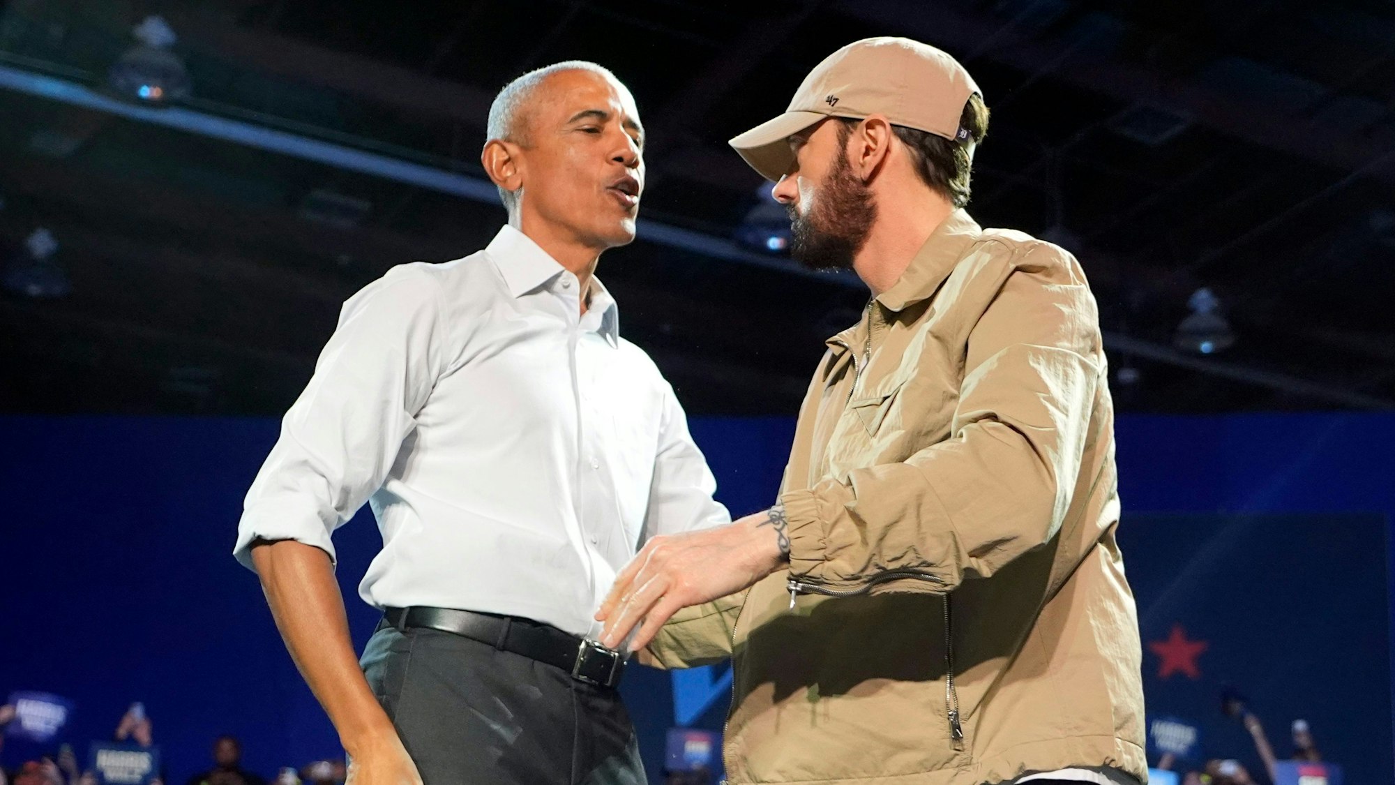 22.10.2024, USA, Detroit: Der Rapper Eminem (r) begrüßt den ehemaligen US-Präsidenten Barack Obama auf der Bühne bei einer Wahlkampfveranstaltung zur Unterstützung der demokratischen US-Präsidentschaftskandidatin Harris. Foto: Paul Sancya/AP/dpa +++ dpa-Bildfunk +++