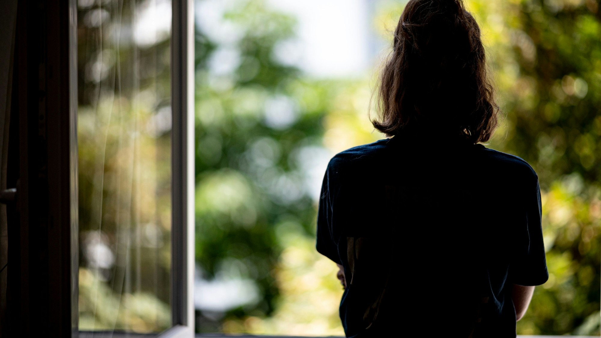 Eine Frau steht in ihrer Wohnung an einem Fenster. (Symbolbild)