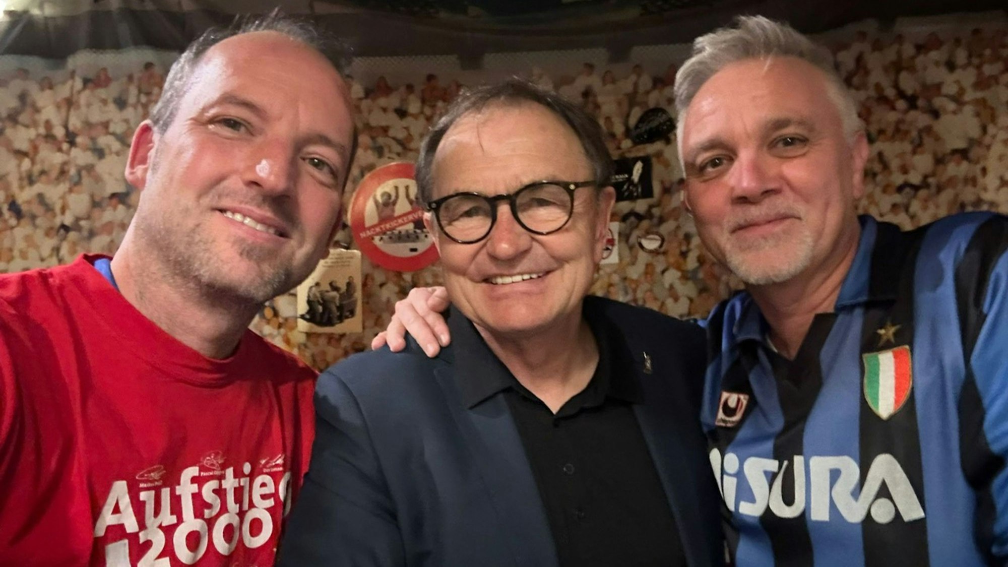 Das Bild zeigt drei Männer, die die Arme umeinander gelegt haben und lächeln.