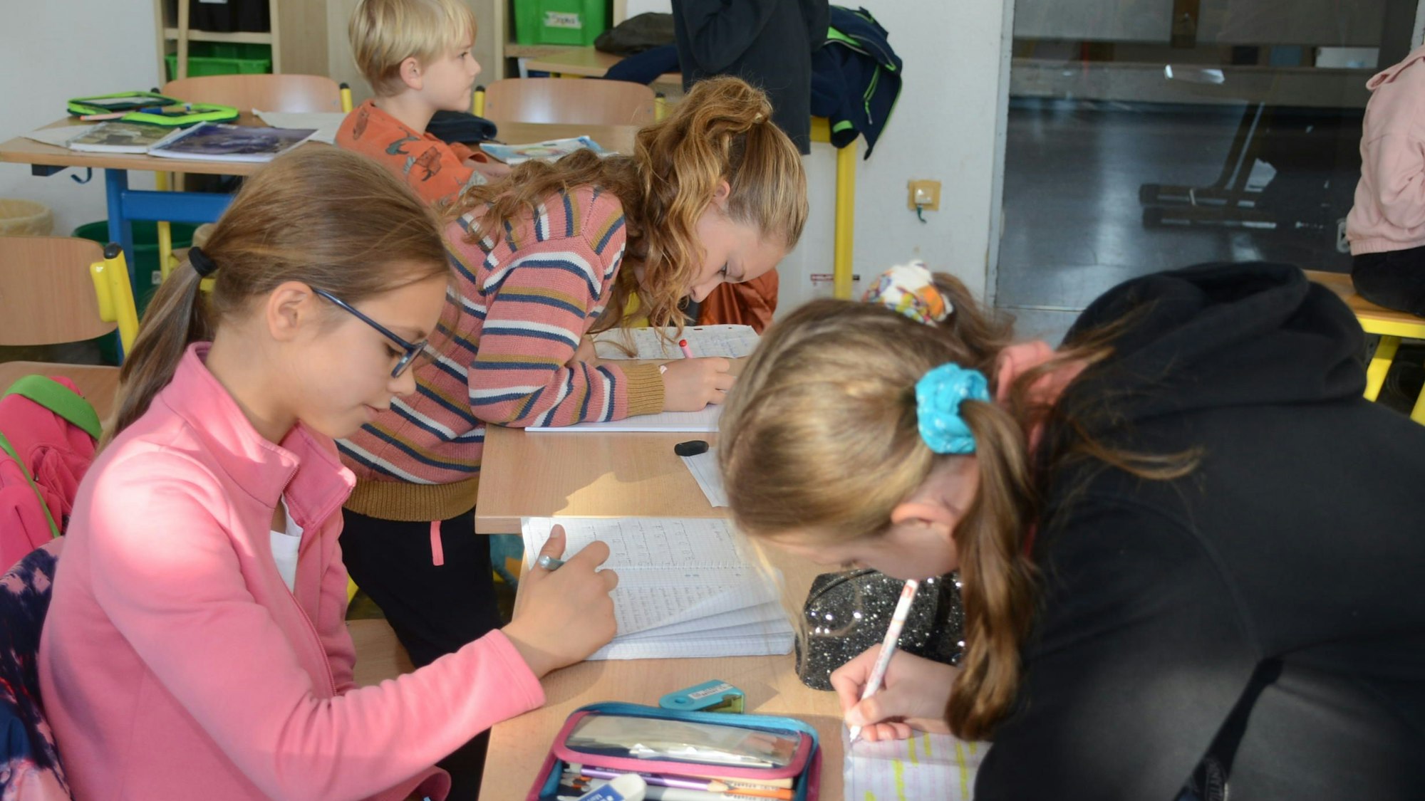 Mädchen sitzen an Schultischen und schreiben in ihre Hefte.