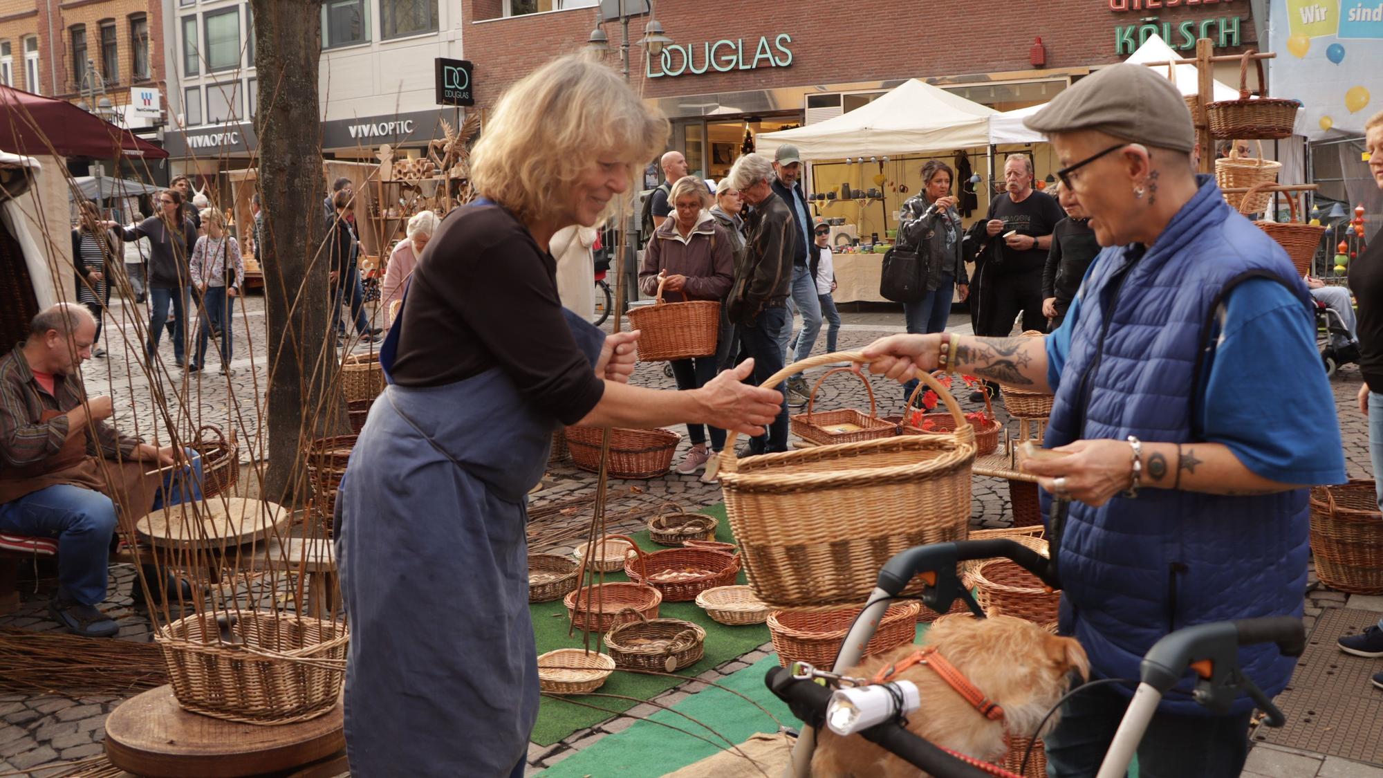 Eine Frau an einem Stand mit geflochtenen Körben überreicht jemandem einen Korb.
