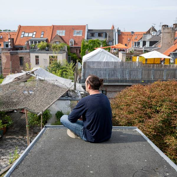Ein Mann sitzt auf einem Flachdach mit Blick auf andere Häuser