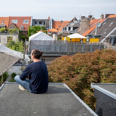 Ein Mann sitzt auf einem Flachdach mit Blick auf andere Häuser