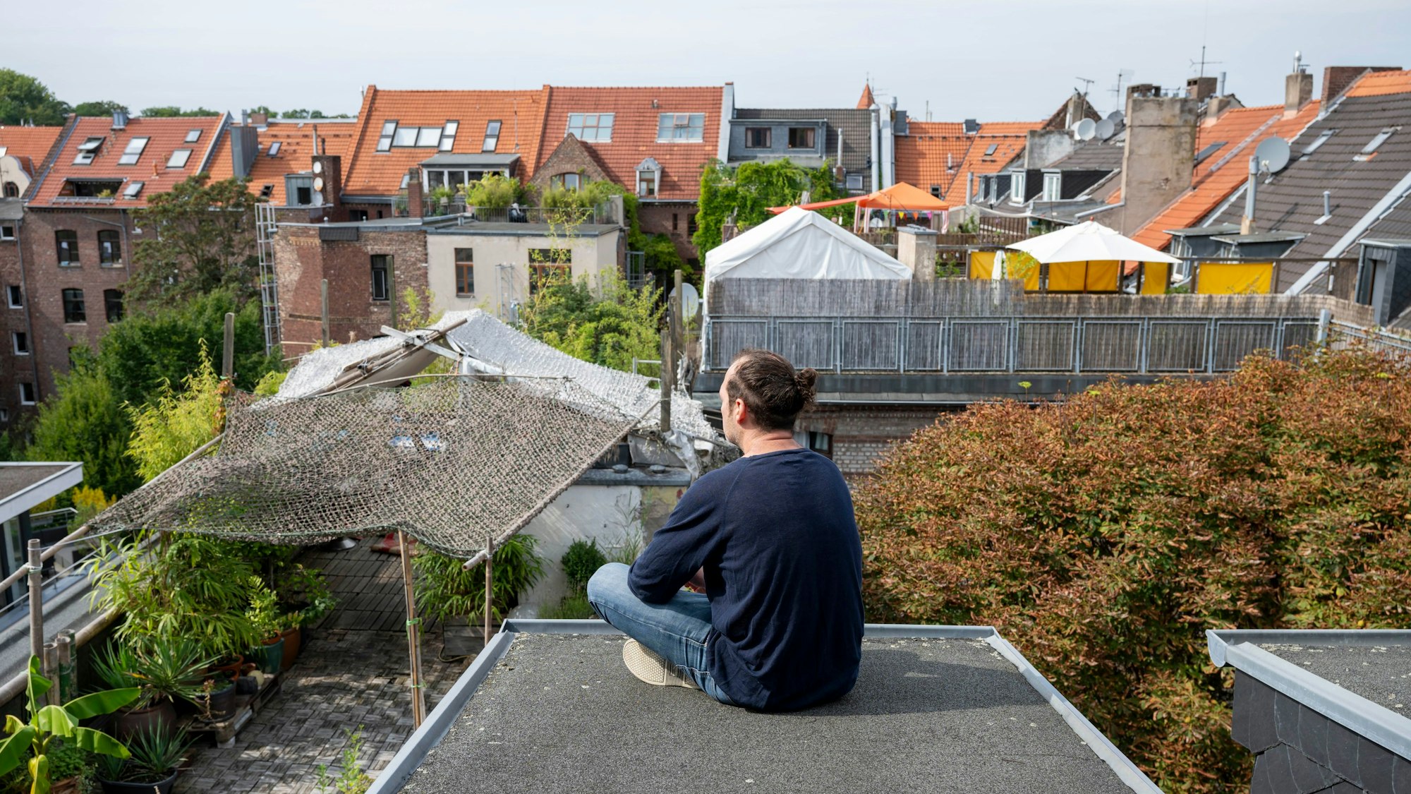 Ein Mann sitzt auf einem Flachdach mit Blick auf andere Häuser