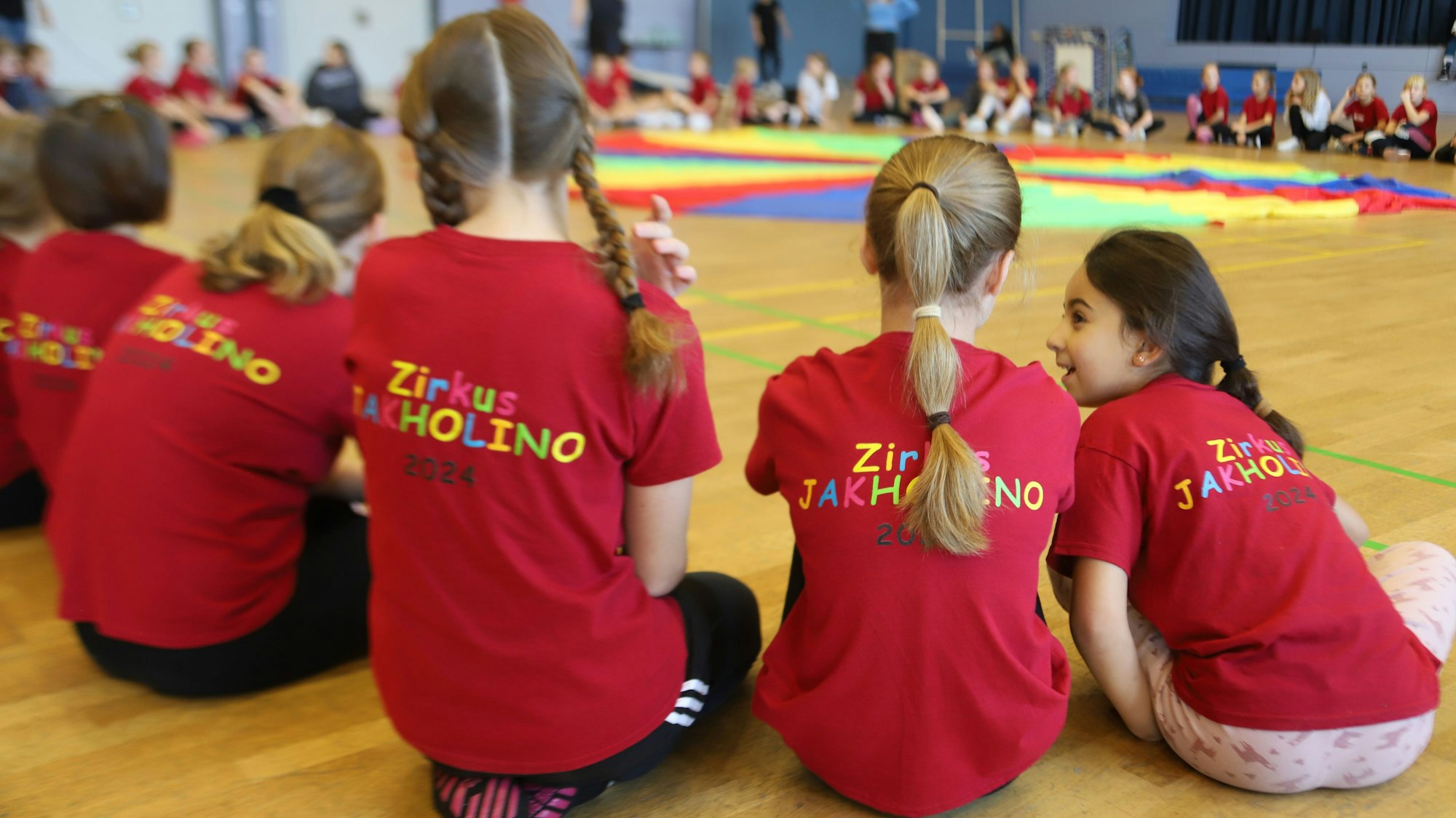 Mädchen sitzen vor einem seidenen Fallschirm in einer Halle.