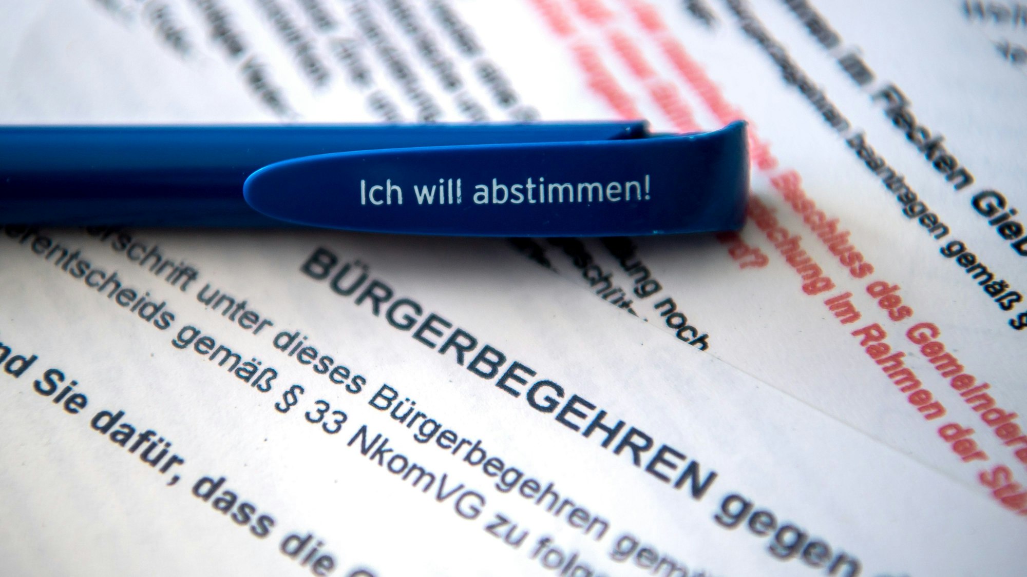 Ein Stift mit der Aufschrift „Ich will abstimmen!“ liegt auf Zetteln mit Bürgerbegehren auf einem Schreibtisch.