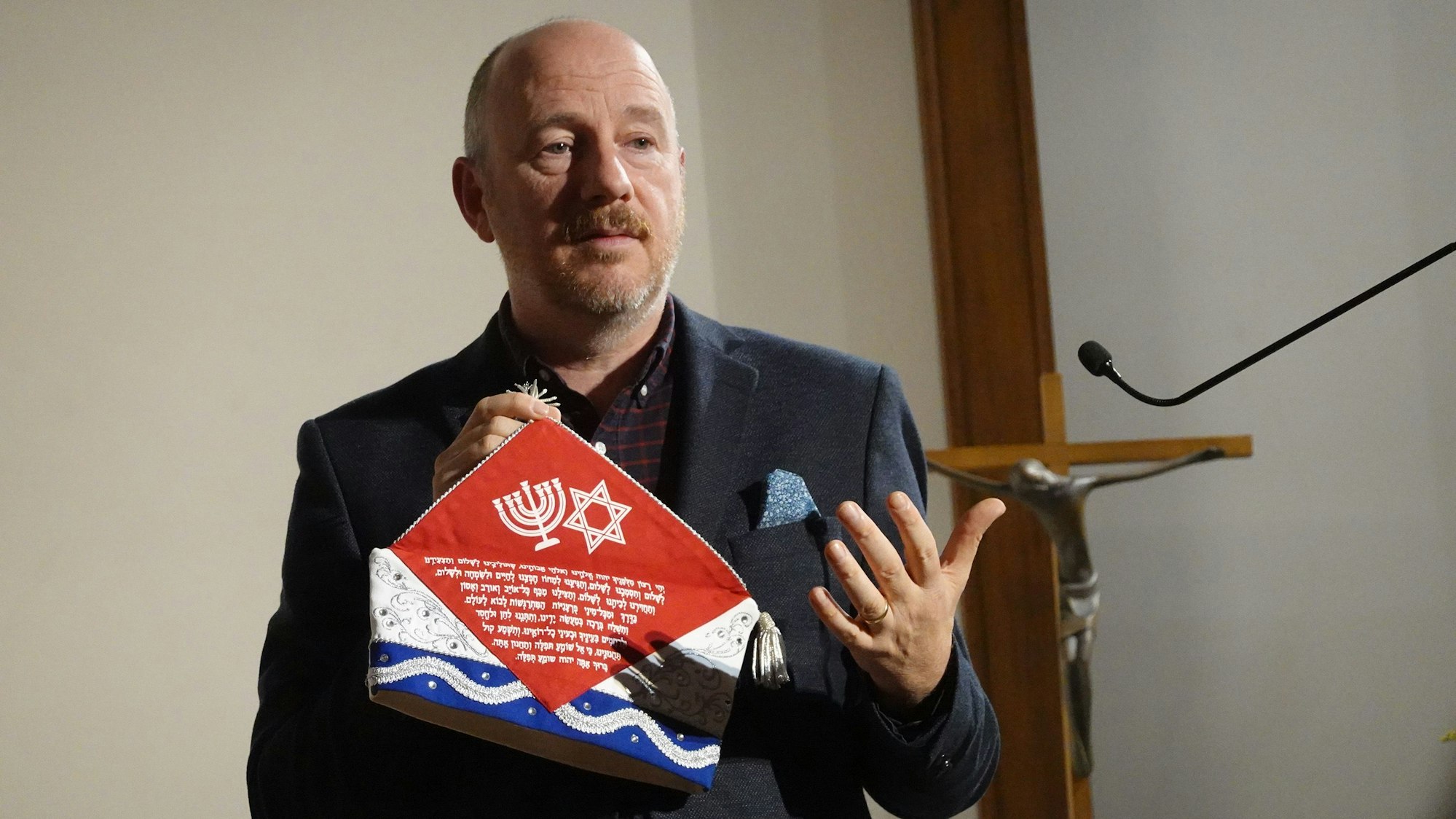 Ein Mann mit einer Kappe in der Hand steht an einem Rednerpult.