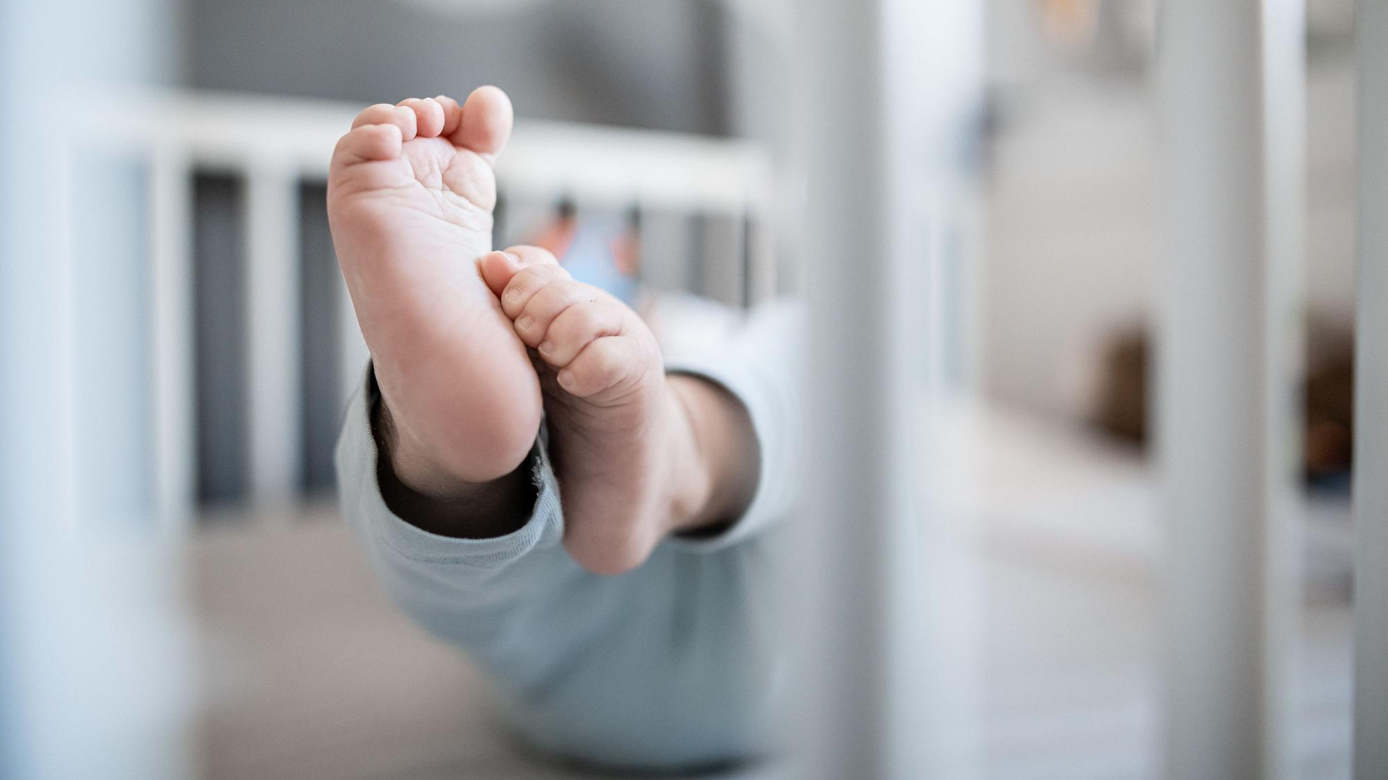 Ein Baby liegt in seinem Bett, lediglich die Füße sind scharf zu erkennen.