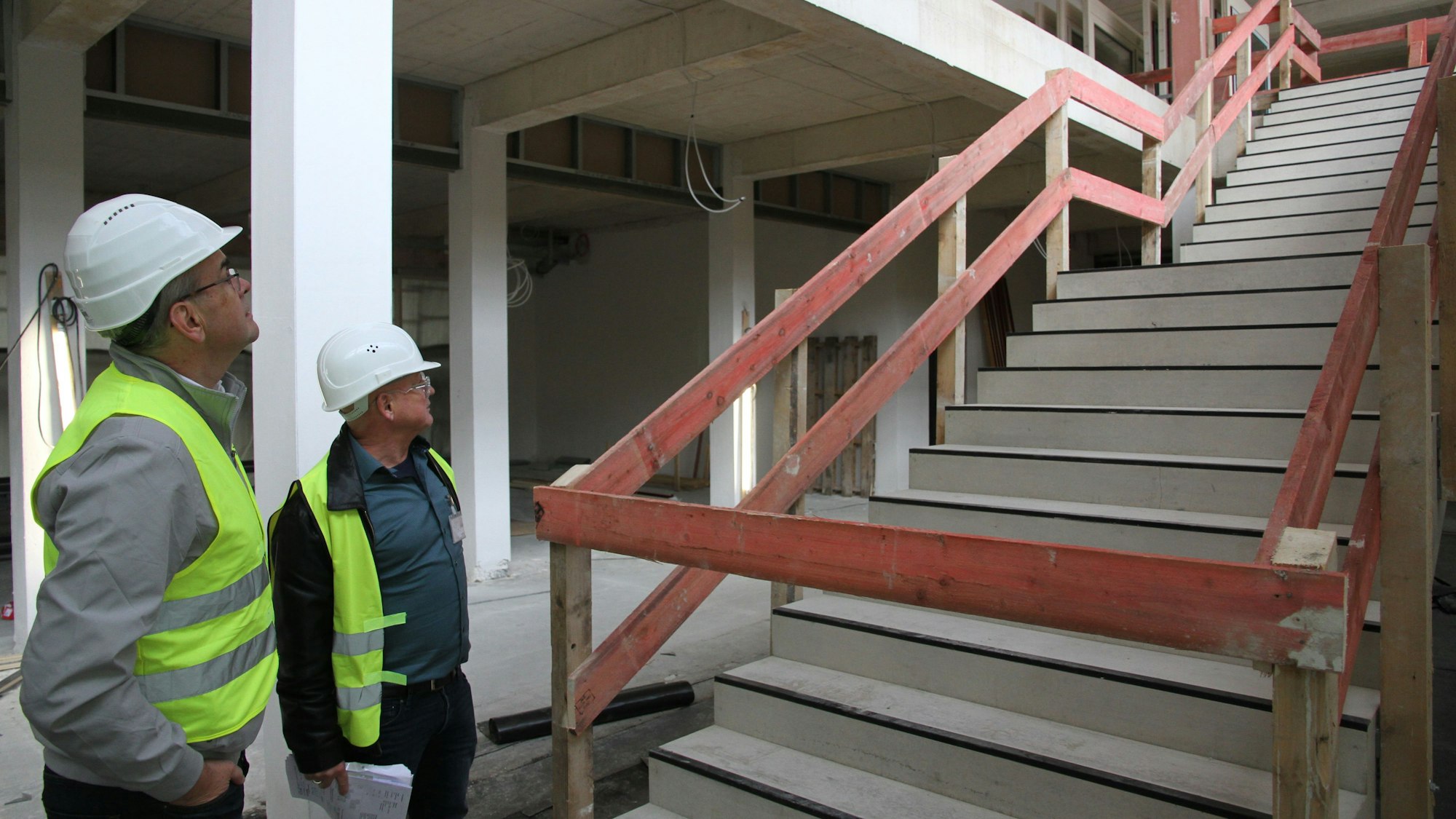 Zwei Männer mit Warnwesten und Bauhelmen neben einer Betontreppe
