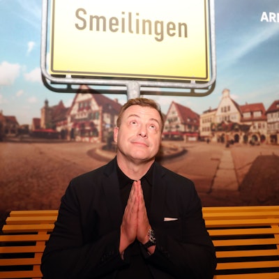 Martin Klempnow sitzt auf einer Bank vor einem Ortsschild, auf dem "Smeilingen" steht.