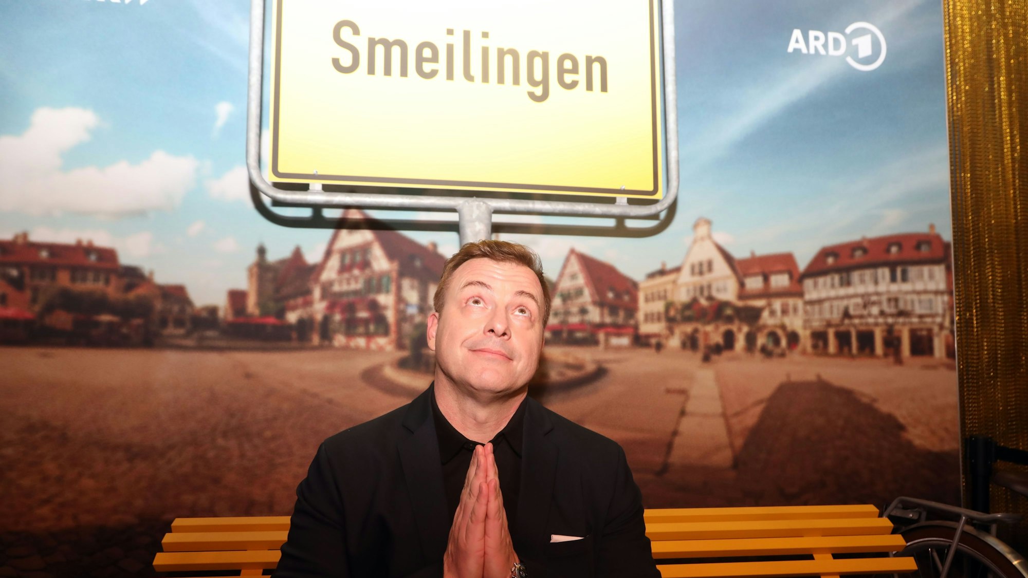 Martin Klempnow sitzt auf einer Bank vor einem Ortsschild, auf dem "Smeilingen" steht.