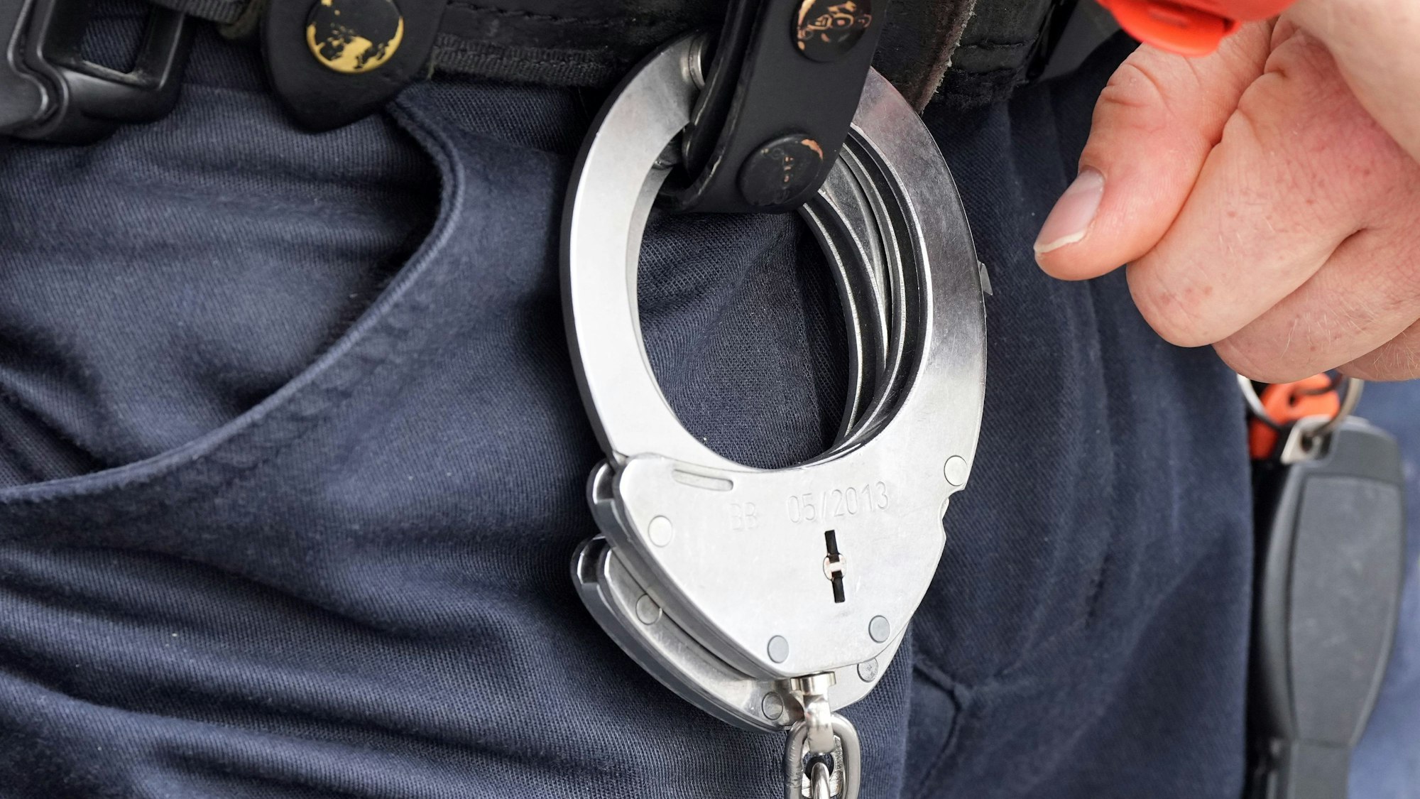Handfesseln aus Metall hängen am Gürtel eines Polizisten.