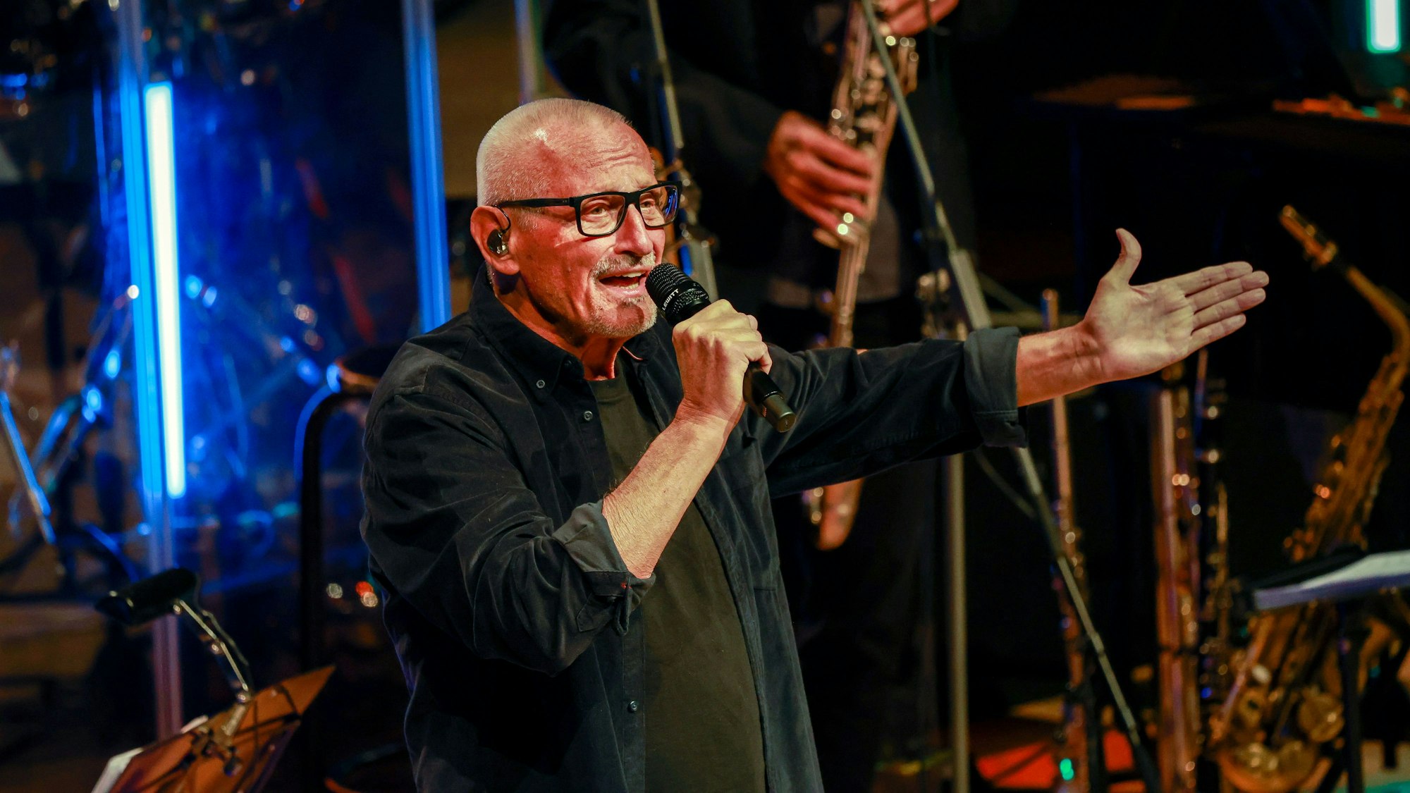 Konstantin Wecker steht in einem schwarzen Hemd auf der Bühne der Kölner Philharmonie und singt in ein Mikrofon.