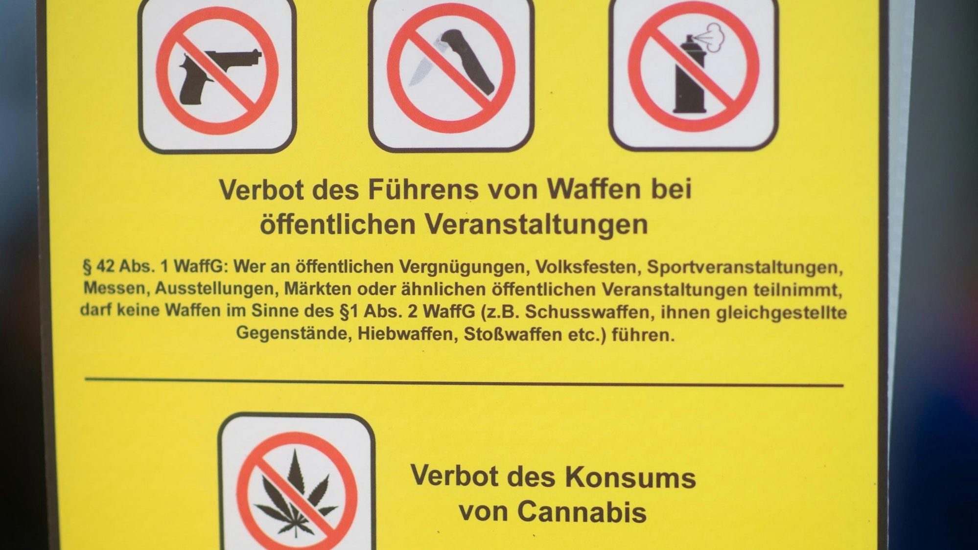 Ein Verbotsschild weist darauf hin, dass keine Waffen zu öffentlichen Veranstaltungen mitgeführt werden dürfen. Auch der Konsum von Cannabis ist in diesem Fall verboten.