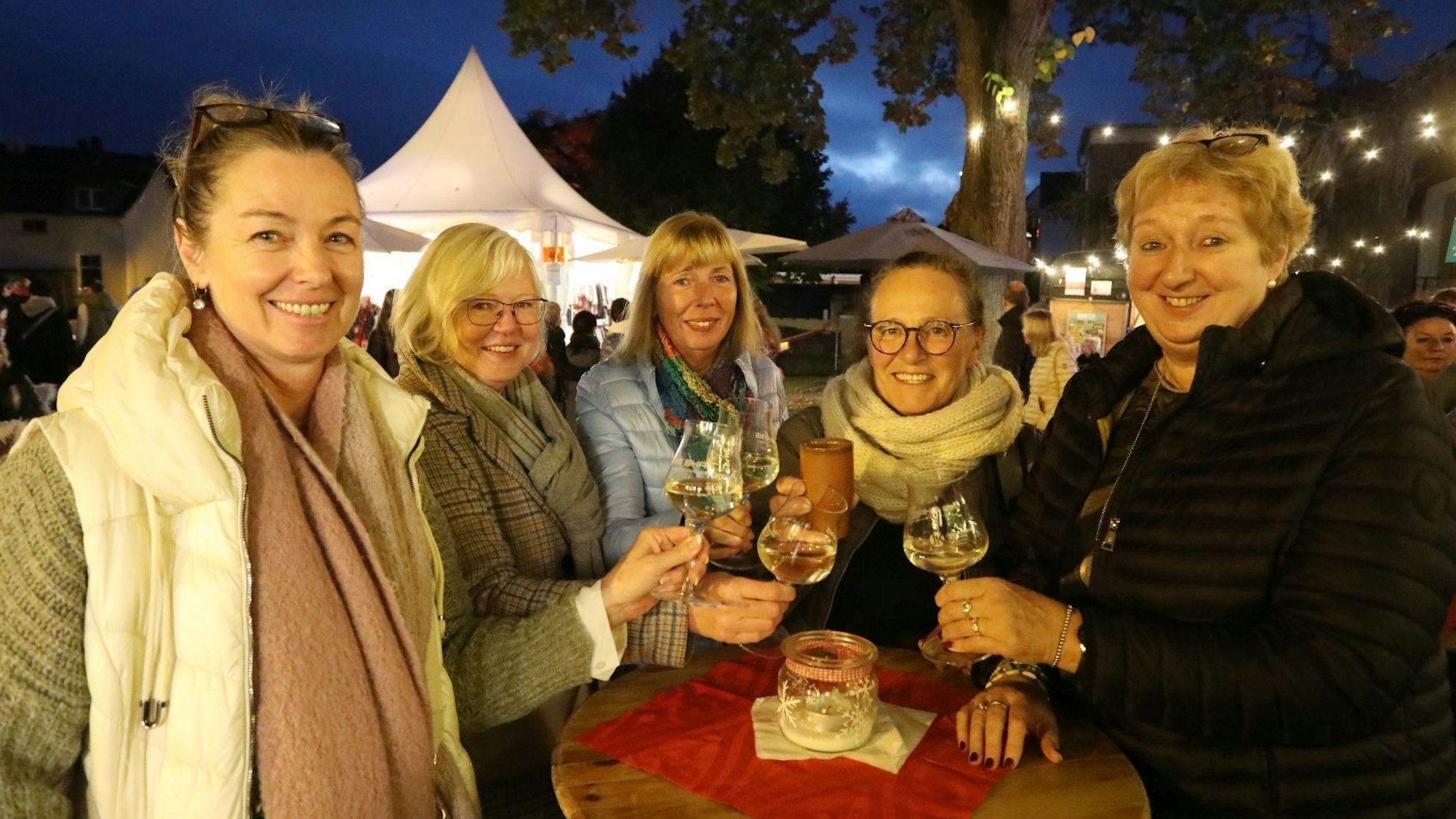 Fünf Frauen stoßen an einem Stehtisch mit ihren Weingläsern an.