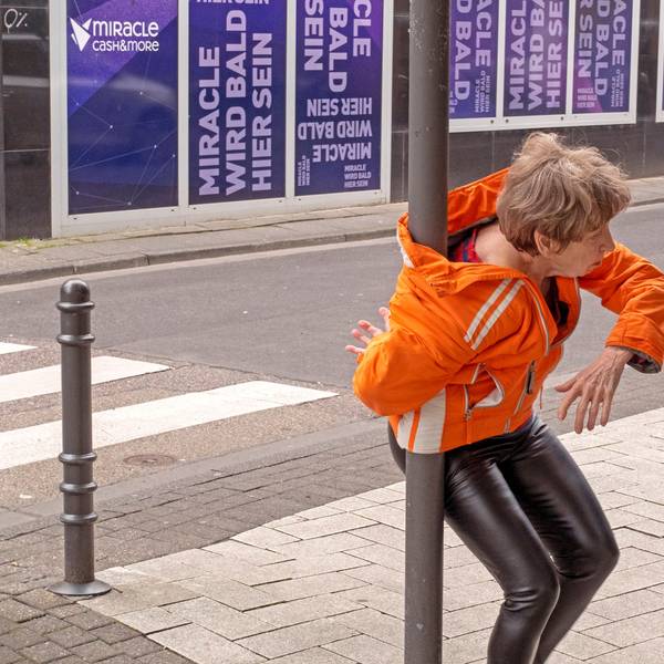 Eine Frau hat sich mit ihrer Jacke um einen Laternenpfahl gewickelt.
