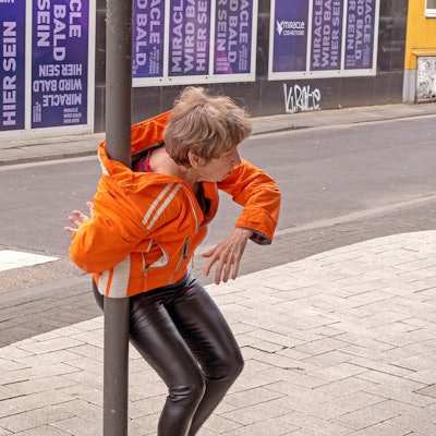 Eine Frau hat sich mit ihrer Jacke um einen Laternenpfahl gewickelt.