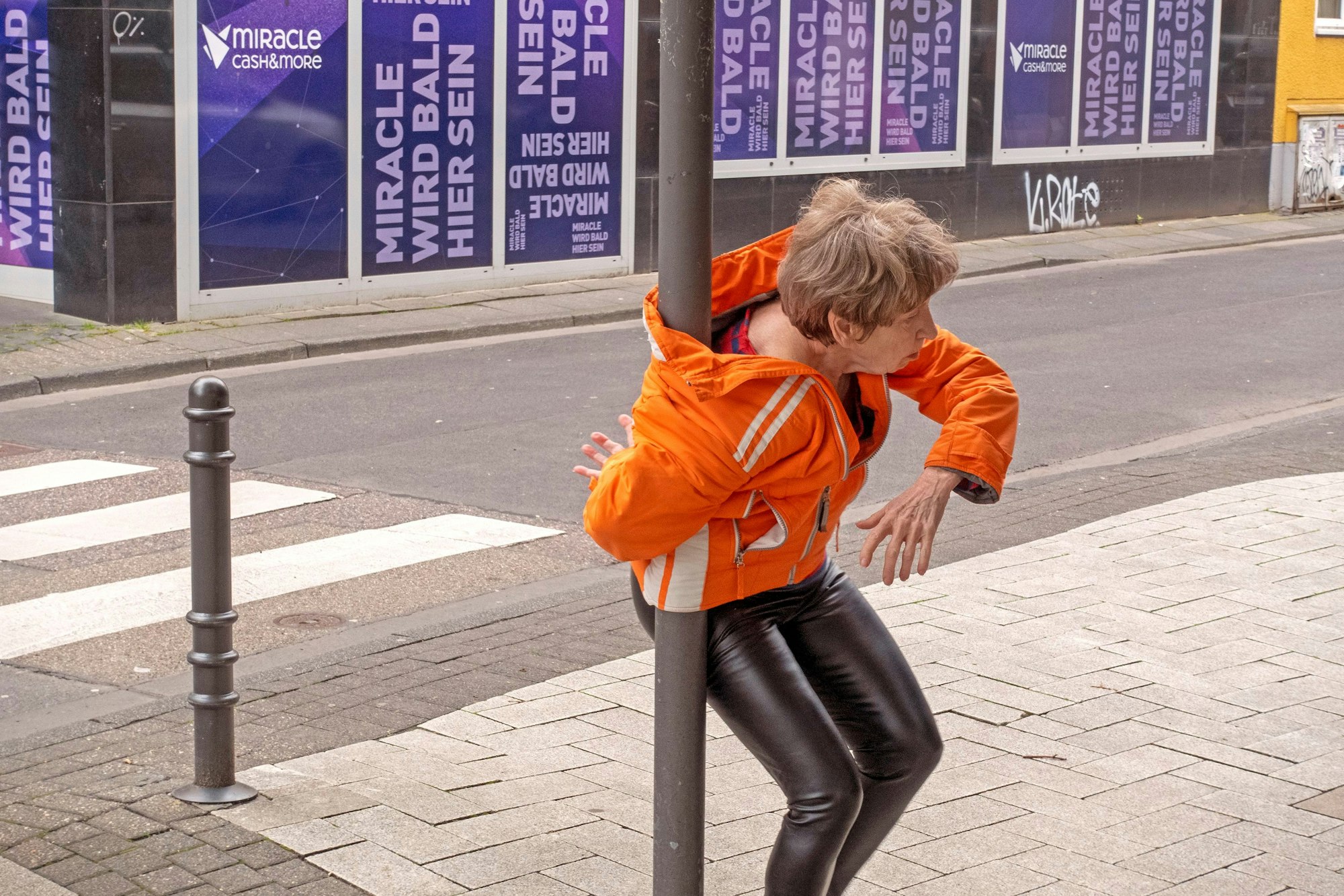 Eine Frau hat sich mit ihrer Jacke um einen Laternenpfahl gewickelt.