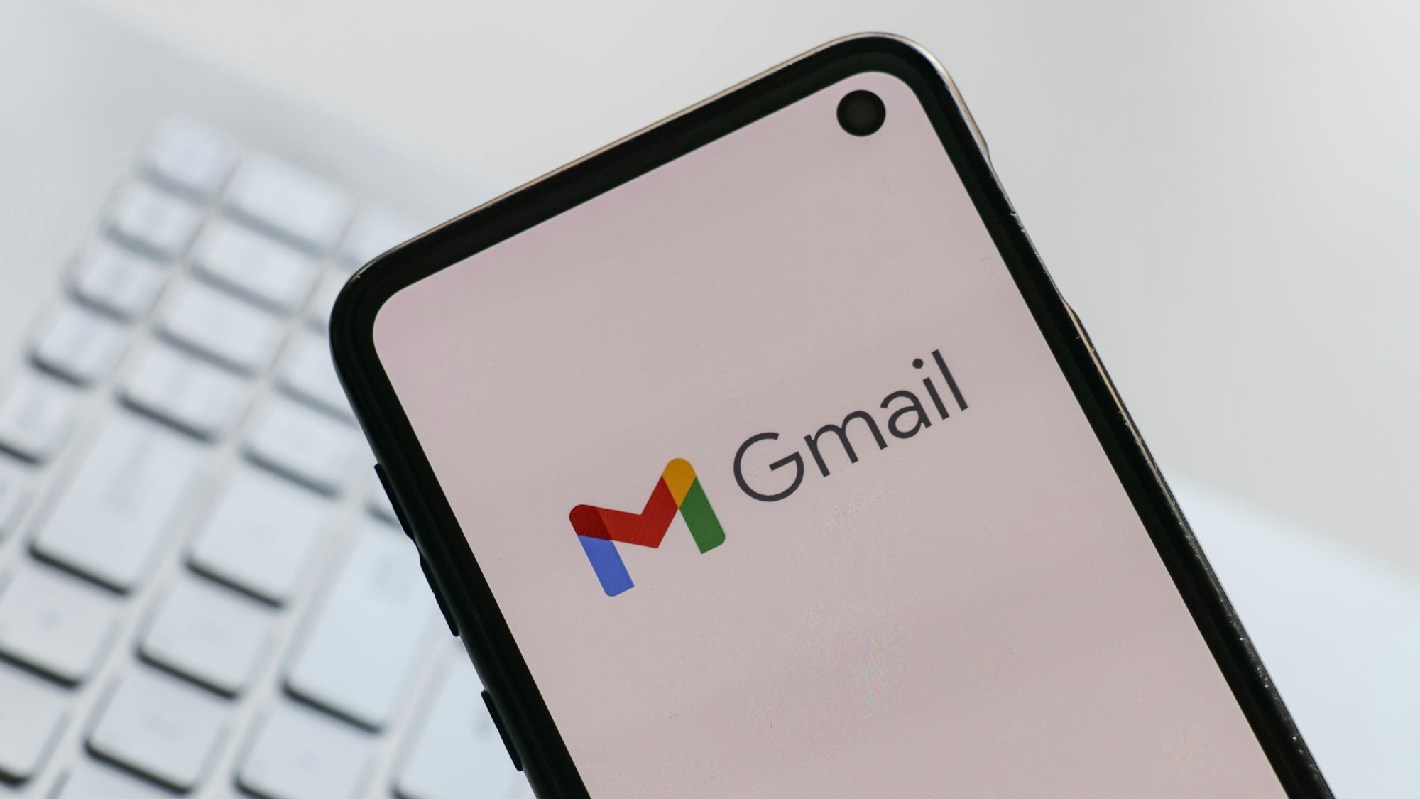 Auf einem Smartphone, das über eine Tastatur gehalten wird, ist das Logo von Gmail zu sehen.