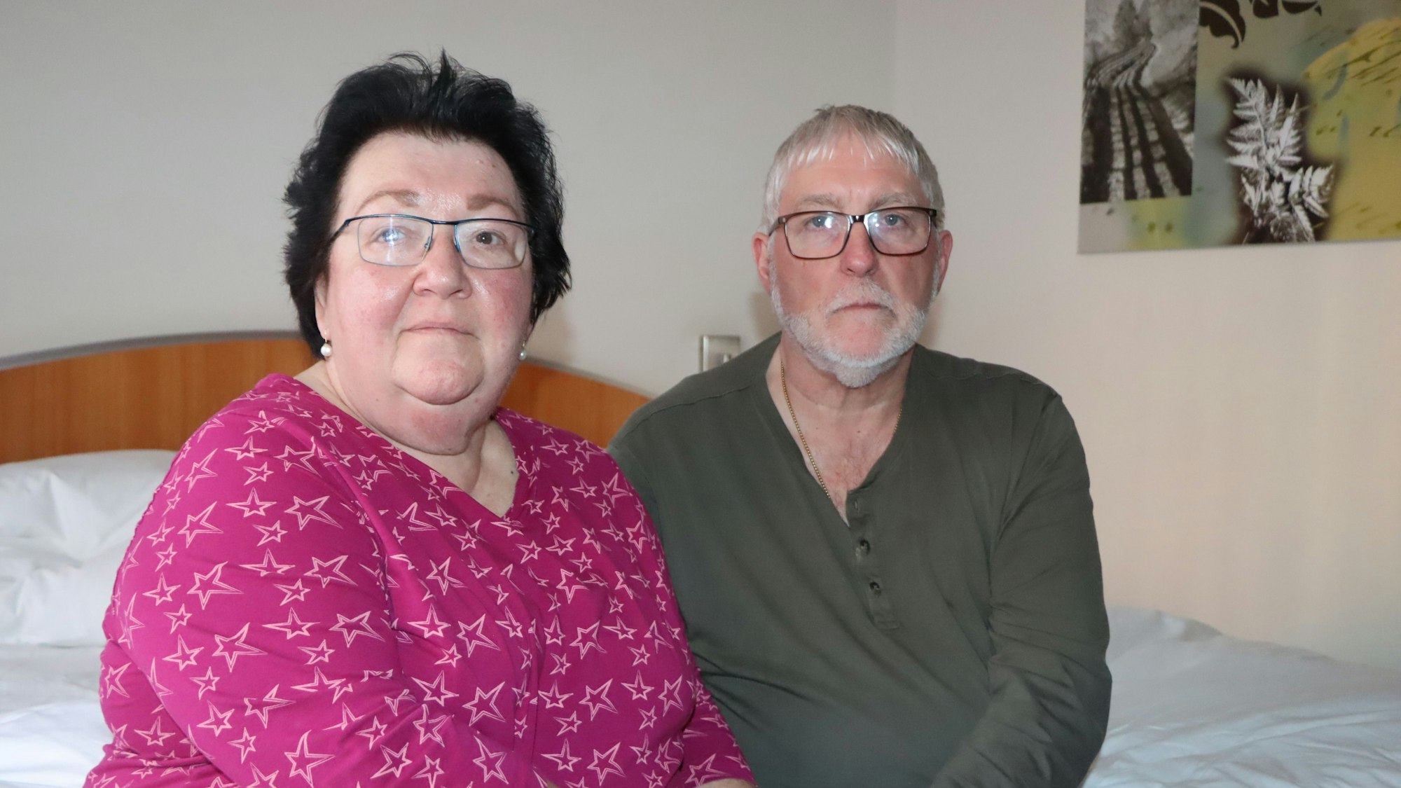 Das Foto zeigt das Ehepaar auf einem Hotelbett sitzend.