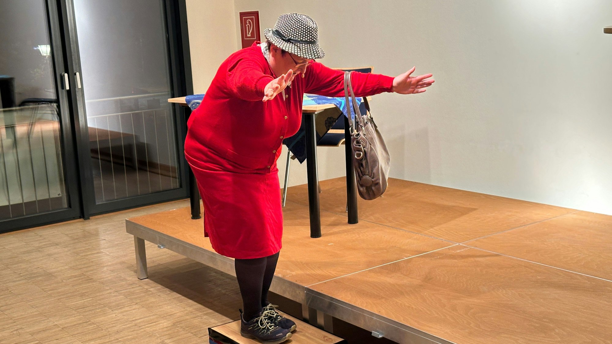 Das Foto zeigt die Kabarettistin Ulrike Böhmer mit einem roten Kleid und einem Pepita-Hut.