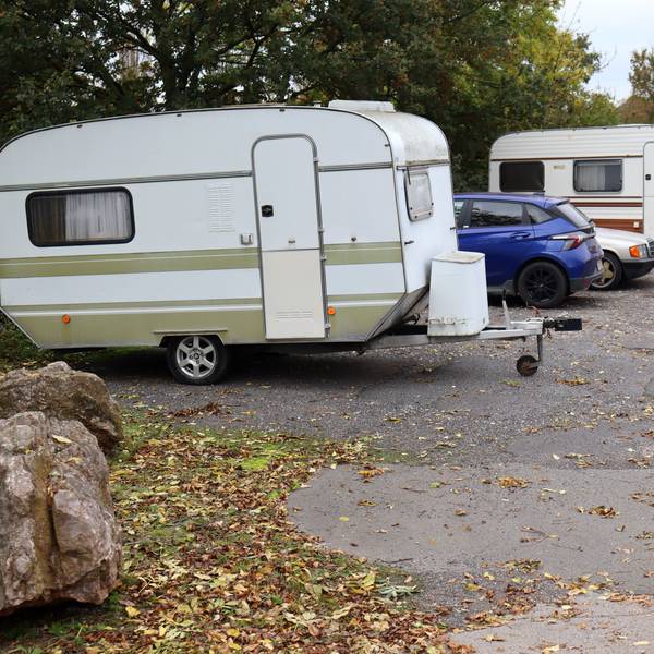Auf einem Park-and-Ride-Platz stehen zwei Wohnwagenanhänger und zwei Autos. Auf dem Boden liegt Laub.