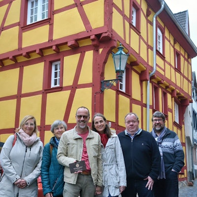 Eine Gruppe Menschen steht vor einem Fachwerkhaus mit gelben Gefachen und roten Balken.