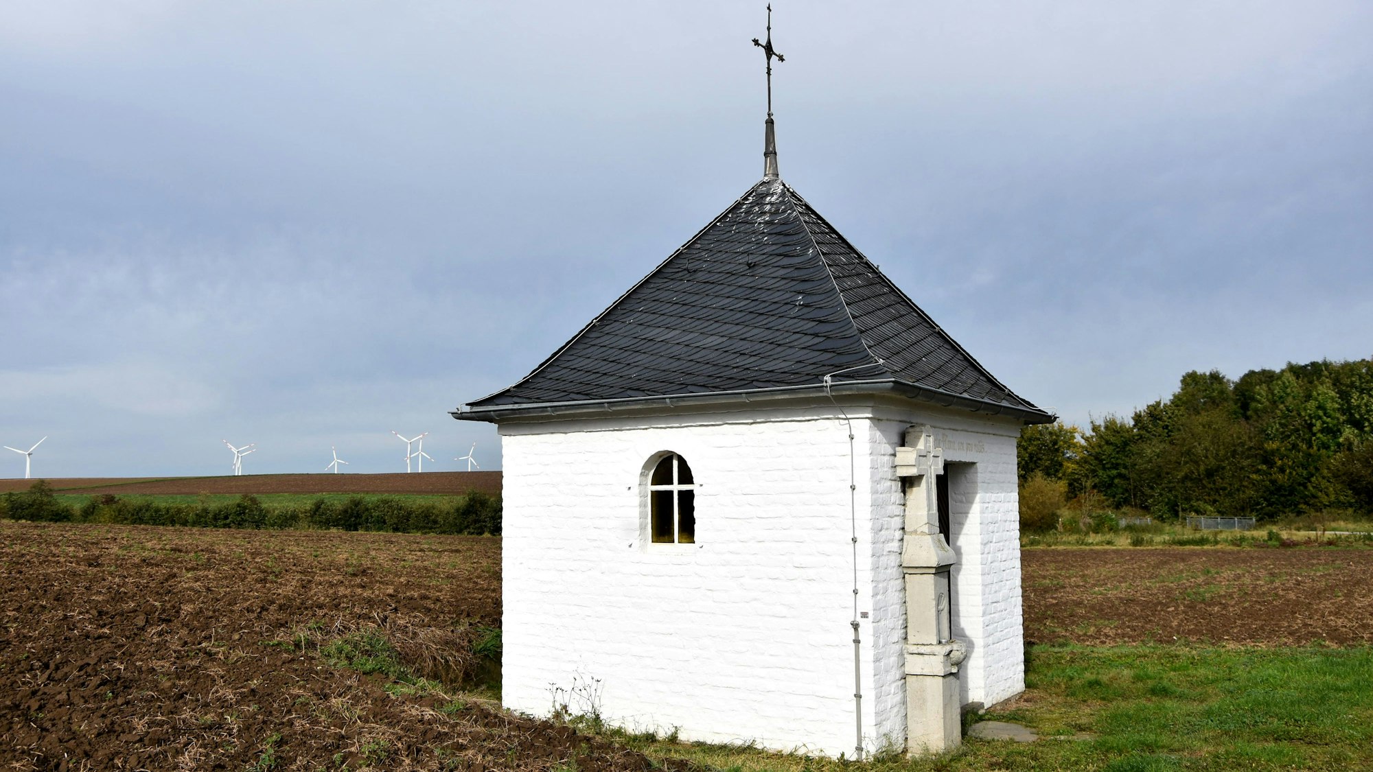 Eine kleine weiße Kapelle steht auf einem Feld.