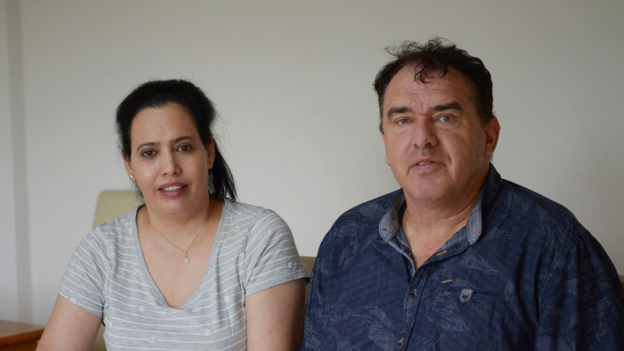 Ein Mann in dunkelblauem Poloshirt und eine Frau in einem grauen T-Shirt sitzen nebeneinander.