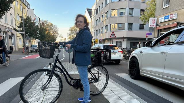 Anwohnerin Monika Bodenstein steht im Oktober 2024 mit Fahrrad auf der Verkehrsinsel Vogelsanger Straße/Sömmeringstraße in Ehrenfeld
