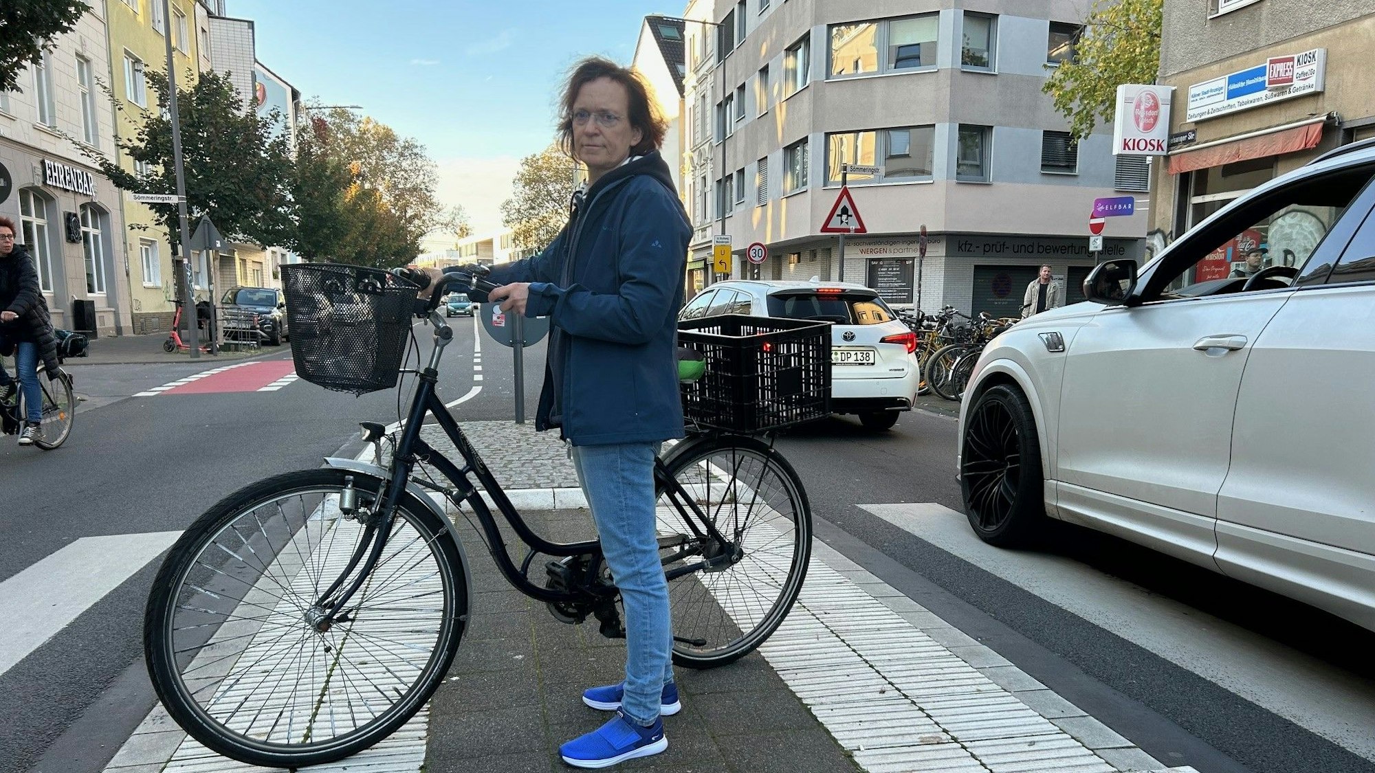 Anwohnerin Monika Bodenstein steht im Oktober 2024 mit Fahrrad auf der Verkehrsinsel Vogelsanger Straße/Sömmeringstraße in Ehrenfeld