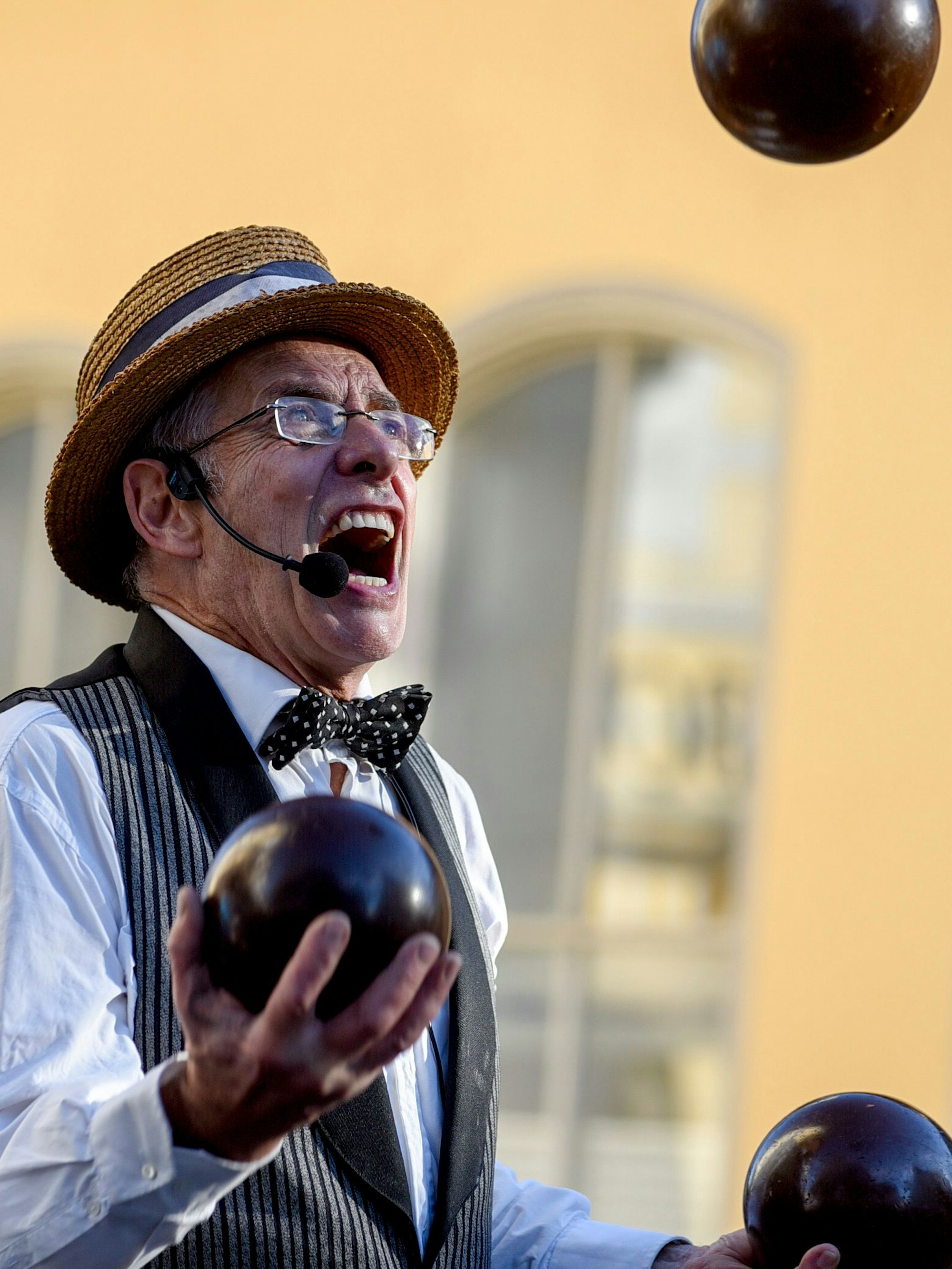 Der Jongleur trägt eine Weste, eine Fliege und einen Hut, während der drei Kugeln in der Luft hält.