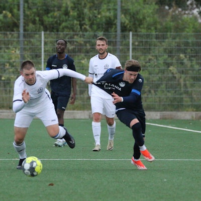 Ein Fußballspieler zieht seinem Gegenspieler beim Kampf um den Ball am Trikot.