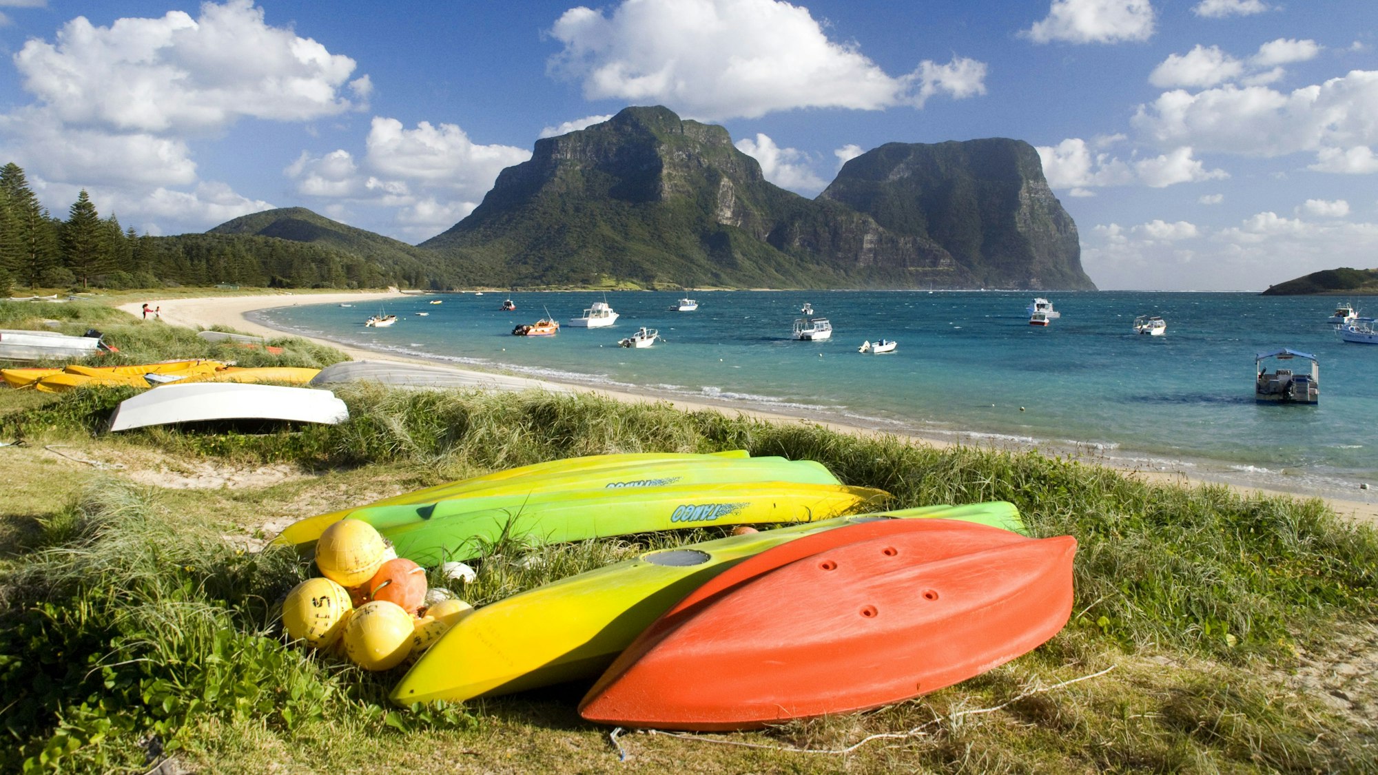 Am Strand von Lord Howe Island liegen zahlreiche Boote, während im Hintergrund die markanten Berge der Insel aufragen.