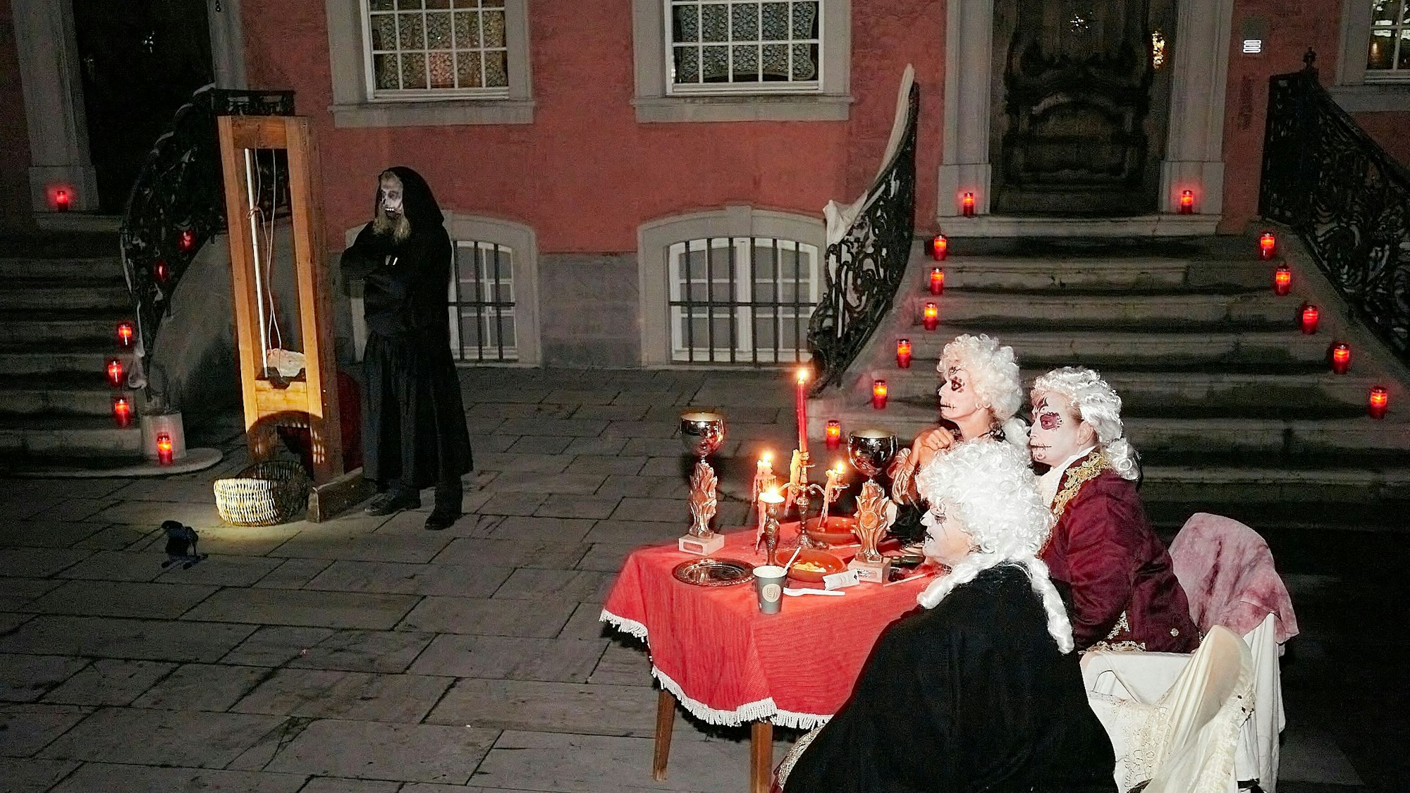 Die gruseligen Gestalten haben an einem dekorierten Tisch vor dem roten Haus Platz genommen und warten auf die Hinrichtung.