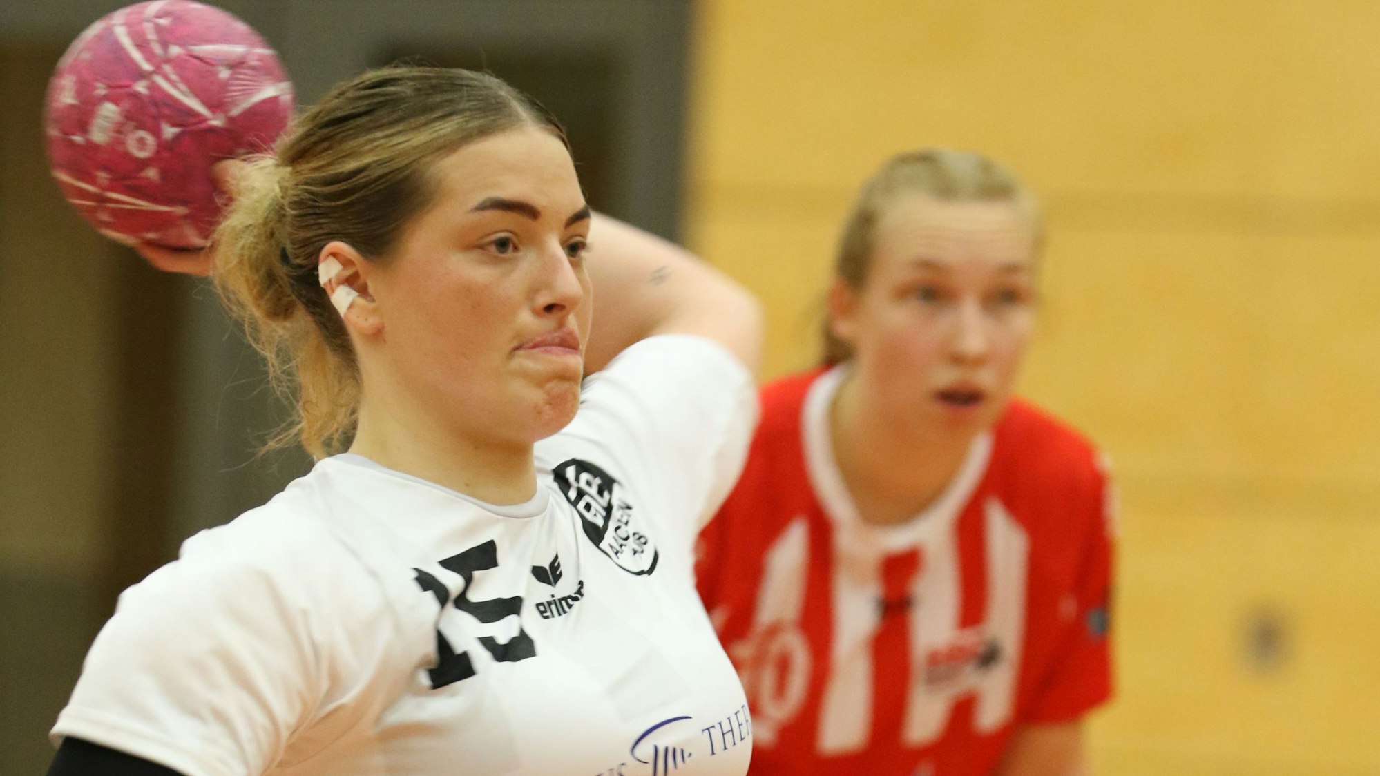 Eine Handballerin beim Pass. Der Ball ist hinter ihrem Kopf, Schmuck im rechten Ohr ist abgeklebt.