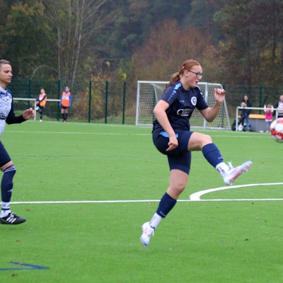 Eine Fußballerin chippt einen Ball über die herannahene Torhüterin.