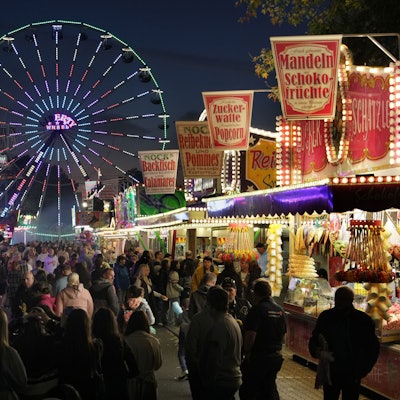 Eine Menschenmenge besucht die beleuchteten Stände, in denen Zuckerwatte, Backfisch und Popcorn verkauft werden.
