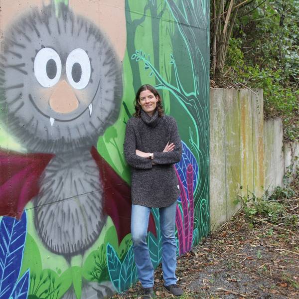 Eine Frau vor einem Graffiti mit einer Fledermaus.