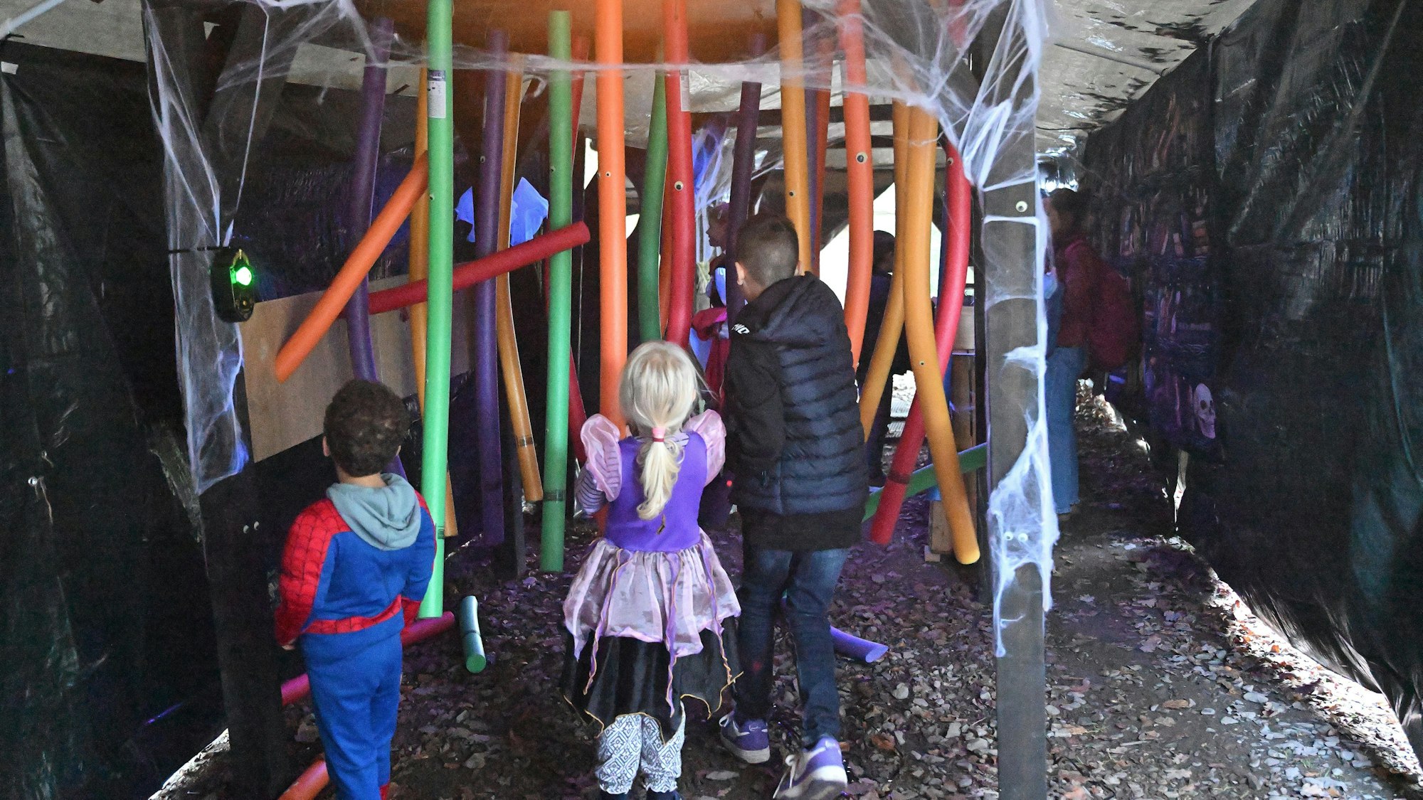 Kinder gehen durch einen Parcours aus Schwimmnudeln in einem abgedunkelten Zelt im Märchenwald Altenberg.